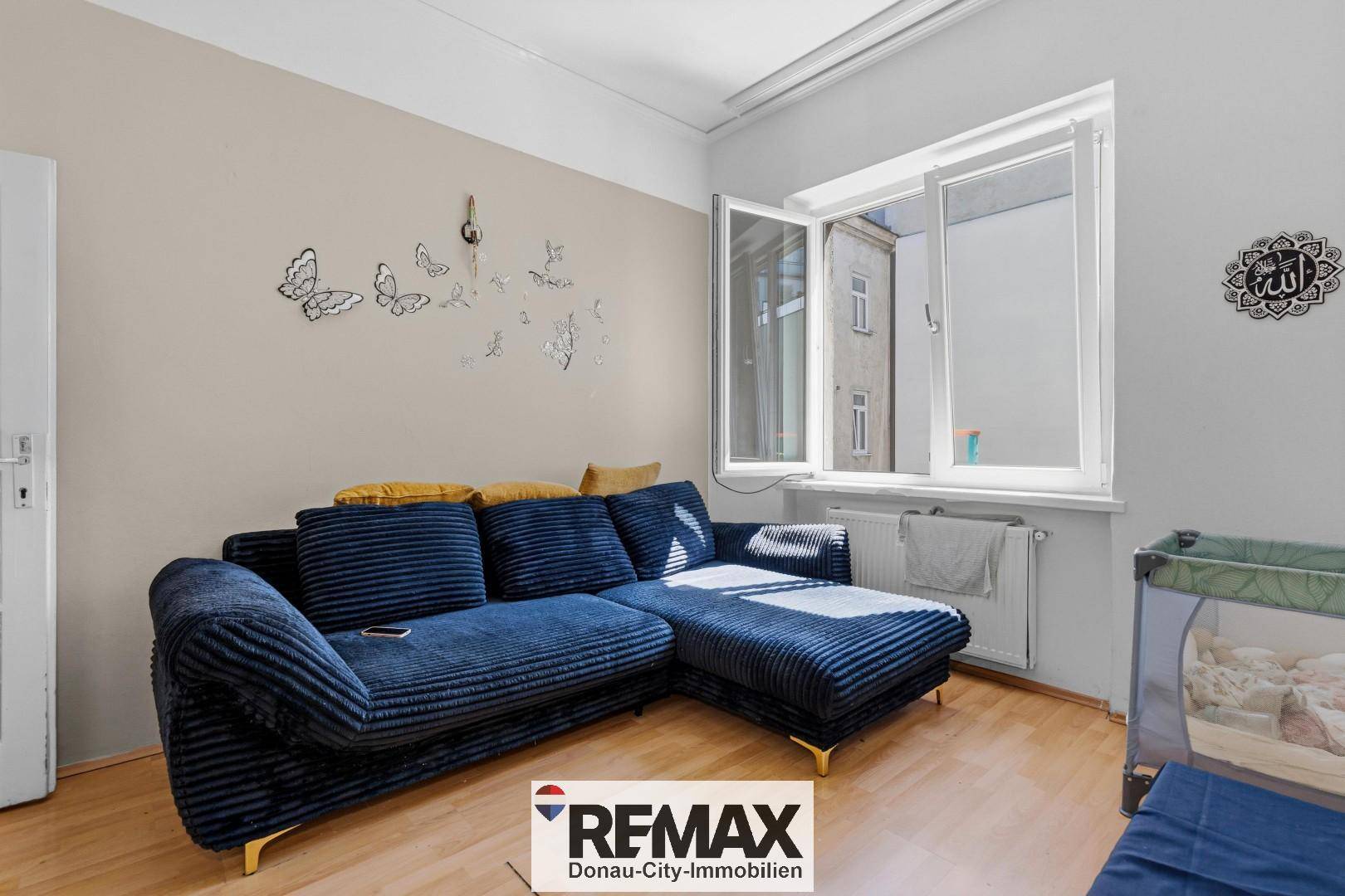 Gemütliches Wohnzimmer mit blauem Sofa, Holzboden und viel Tageslicht durch das Fenster.