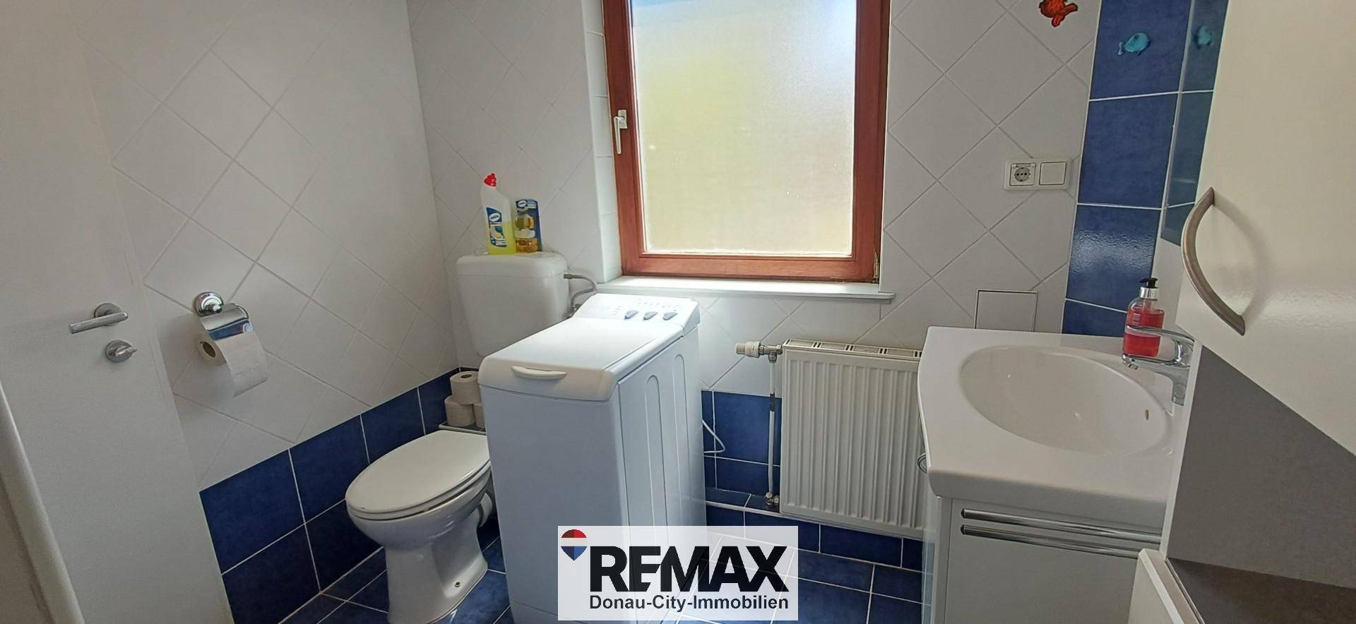 Badezimmer mit WC, Waschbecken, Waschmaschine und blauen Fliesen.