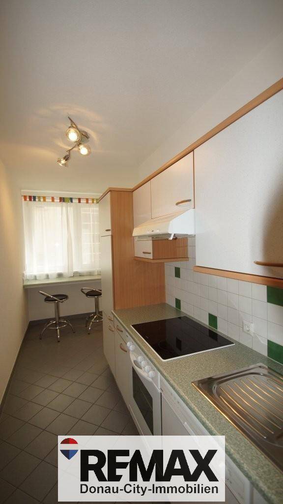 Funktionale Küche mit weißen Schränken, integriertem Backofen und Essbereich am Fenster.