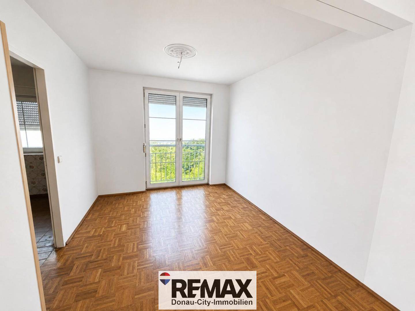 Helles Zimmer mit Parkettboden und Zugang zu einem französischen Balkon, der viel Licht spendet.