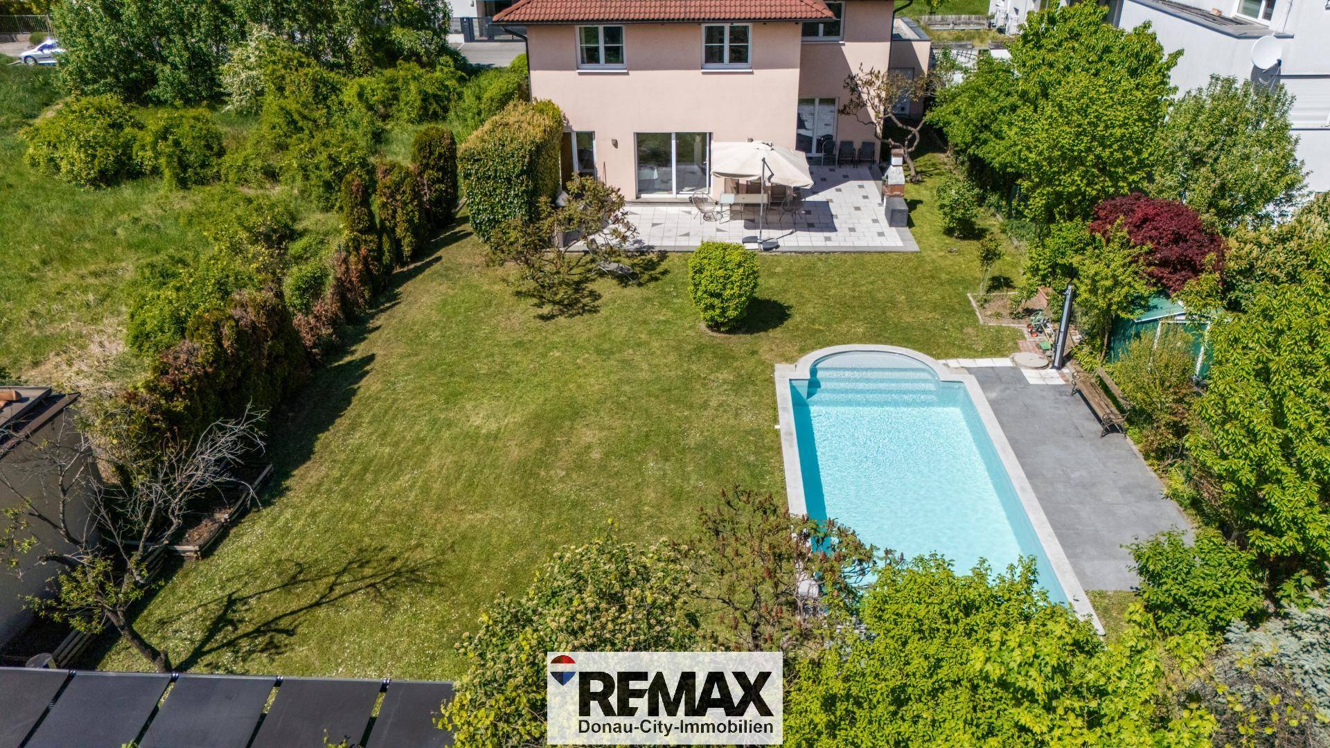 Rückansicht des Hauses mit großer Terrasse, Gartenmöbeln, Rasenfläche und Swimmingpool.