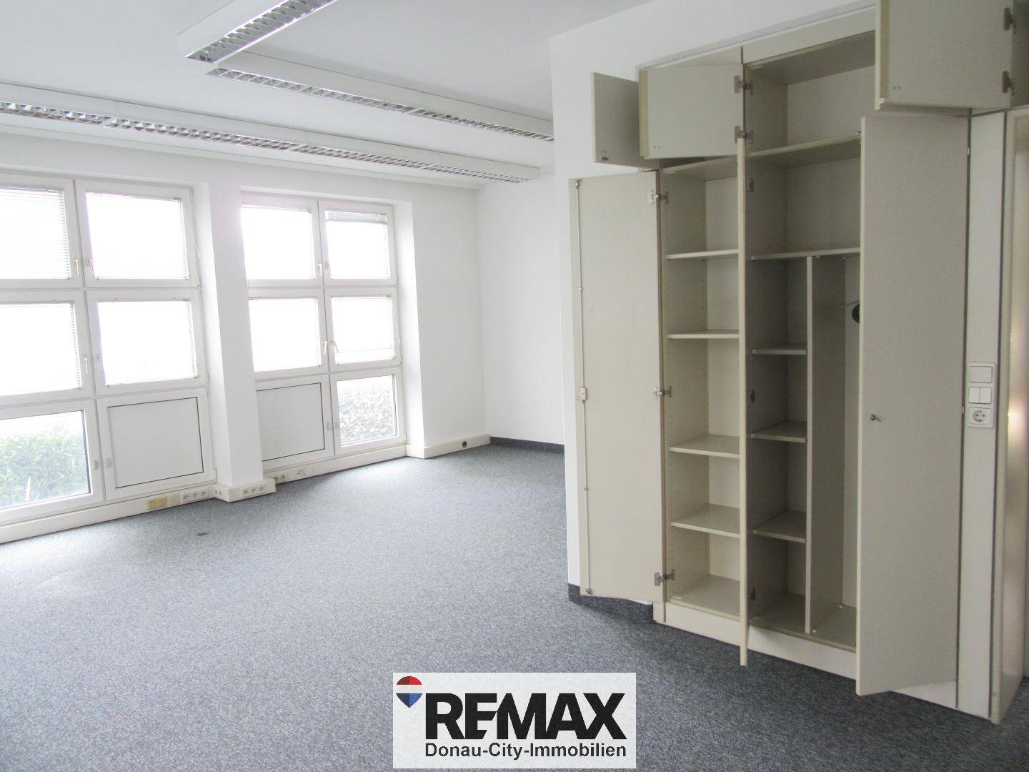 Geräumiges Büro mit Teppichboden, großen Fenstern und praktischen Einbauschränken für Stauraum.