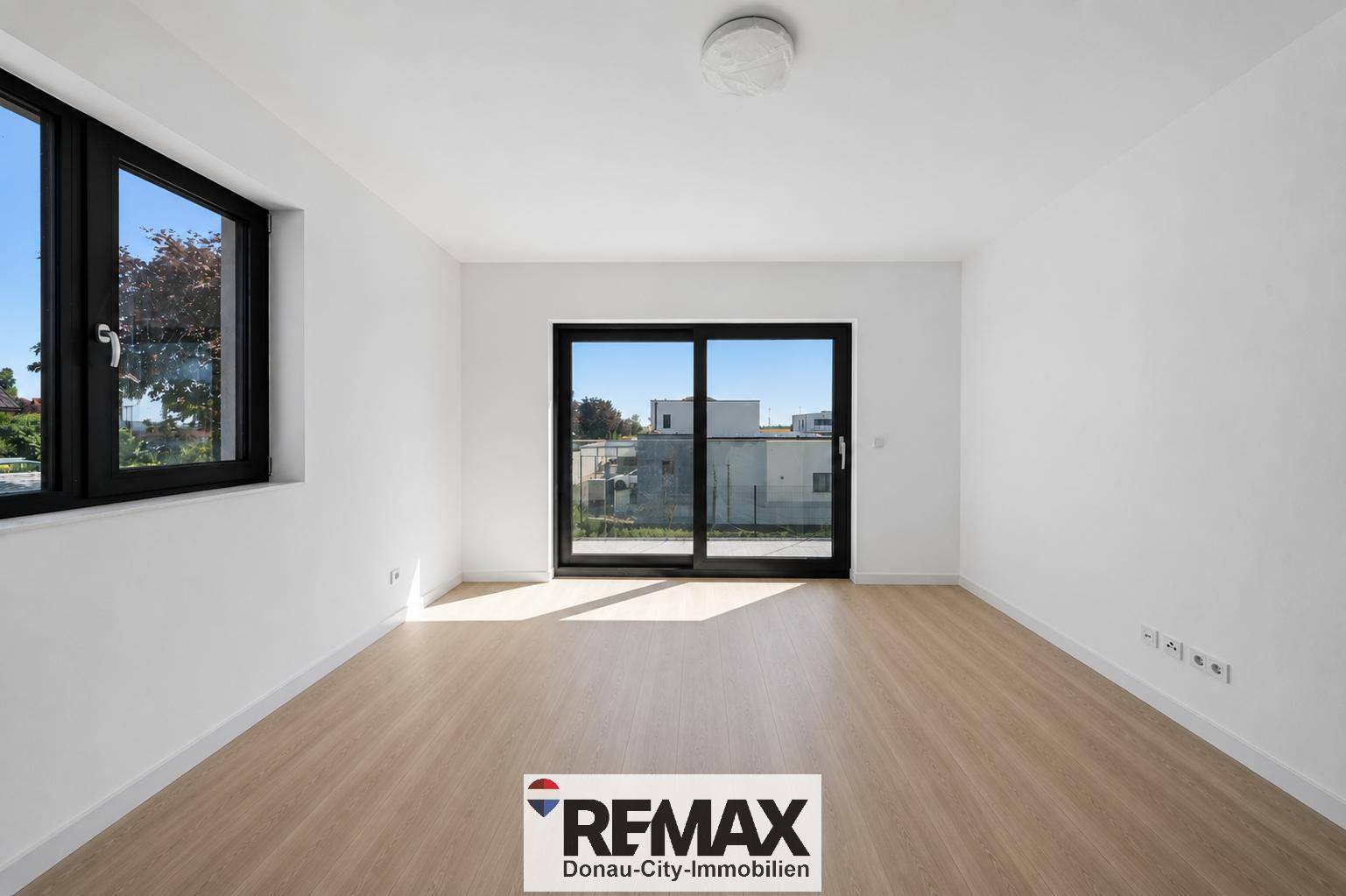 Helles, leeres Schlafzimmer mit Holzboden und Schiebetür zum Balkon.