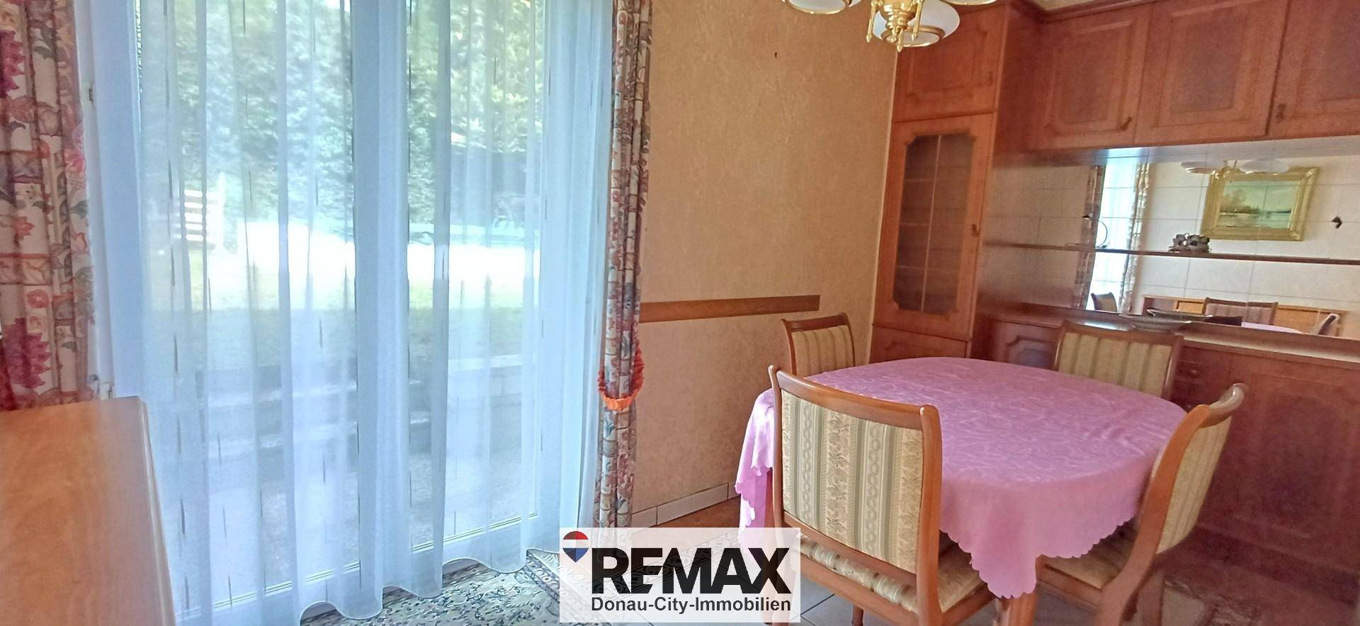 Essbereich mit rundem Tisch und Stühlen, direkt neben einem großen Fenster mit Vorhängen.