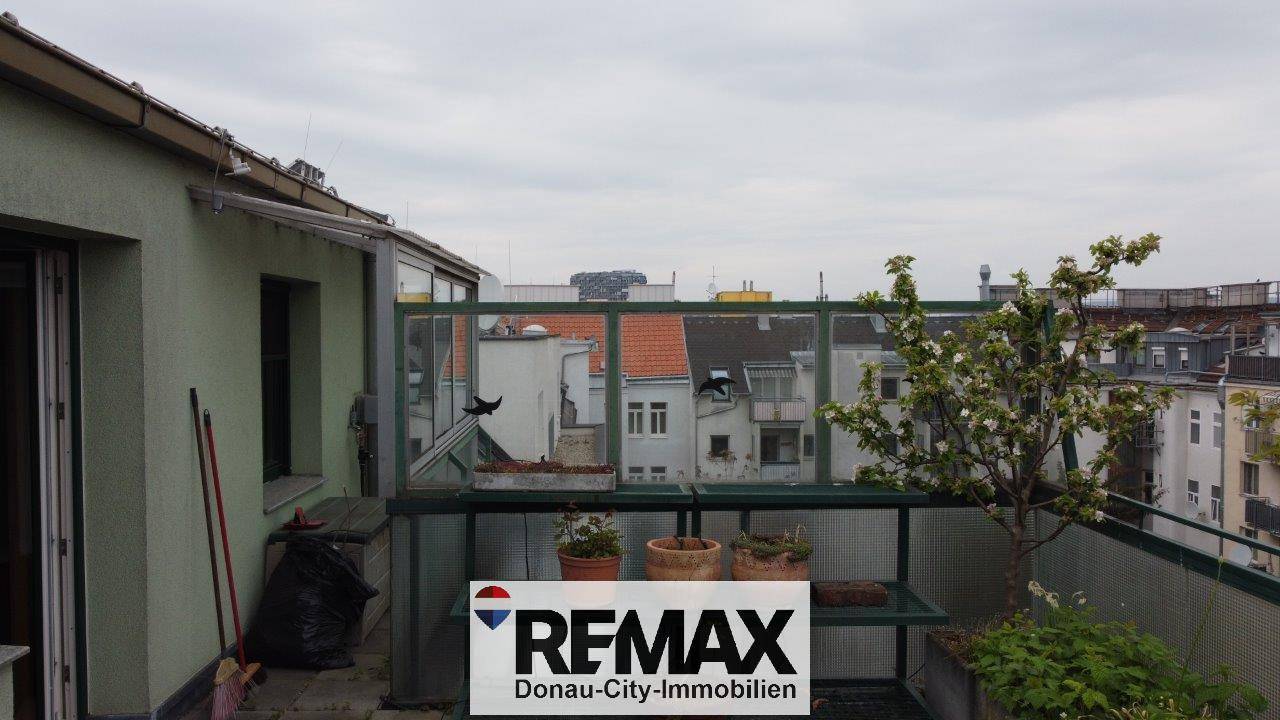 Balkon mit Glasgeländer, Pflanzen und Ausblick auf die städtische Umgebung.