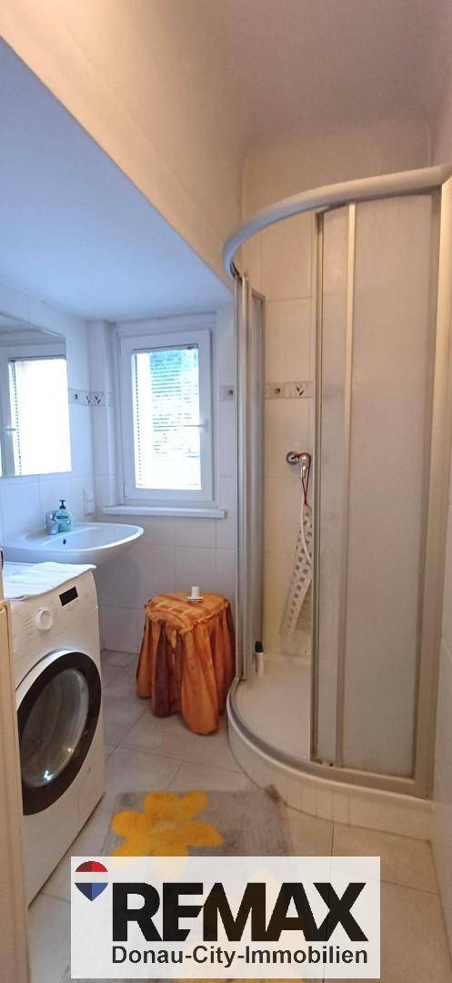 Badezimmer mit Duschkabine, Waschbecken, Waschmaschine und einem Fenster für natürliches Licht.