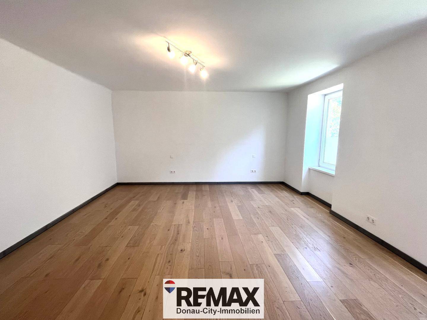 Heller, leerer Raum mit Holzboden und einem Fenster, ideal als Wohnzimmer nutzbar.