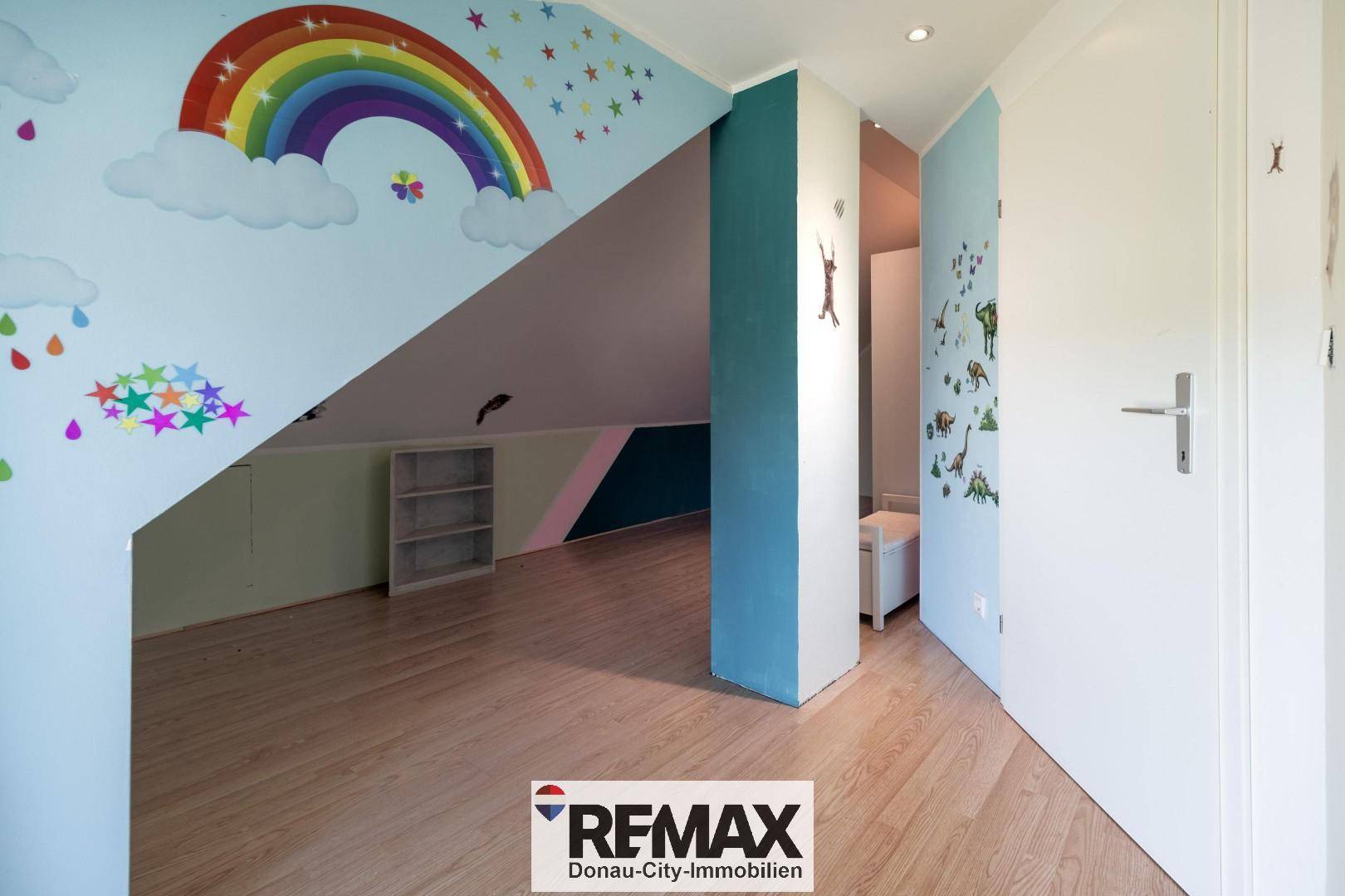 Farbenfrohes Dachzimmer mit Regenbogen-Wandmalerei und schräger Decke, ideal für Kinder.