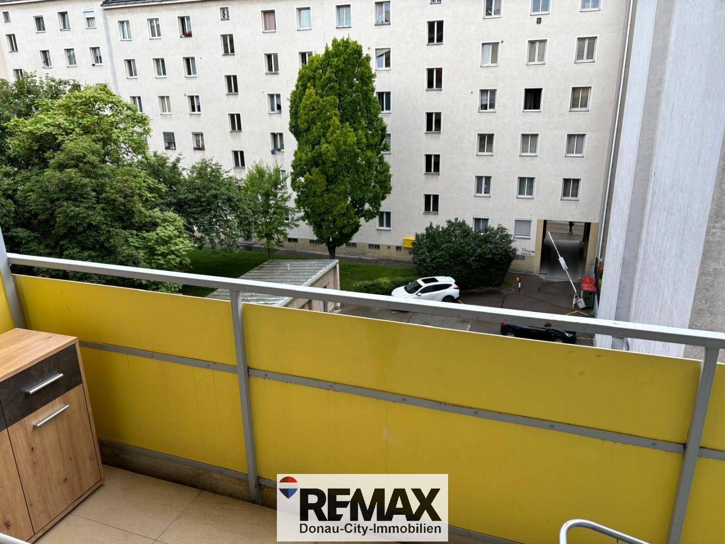 Balkon mit Blick auf den begrünten Innenhof und die umliegenden Wohngebäude.