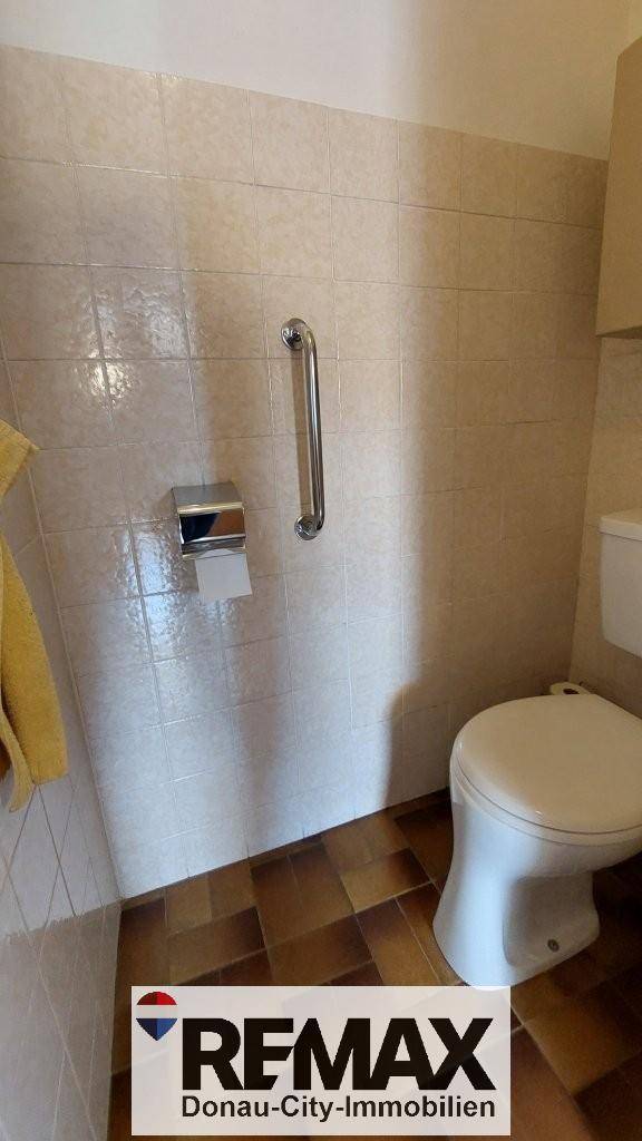 Separate Toilette mit hellen Fliesen und Haltegriff für zusätzliche Sicherheit.