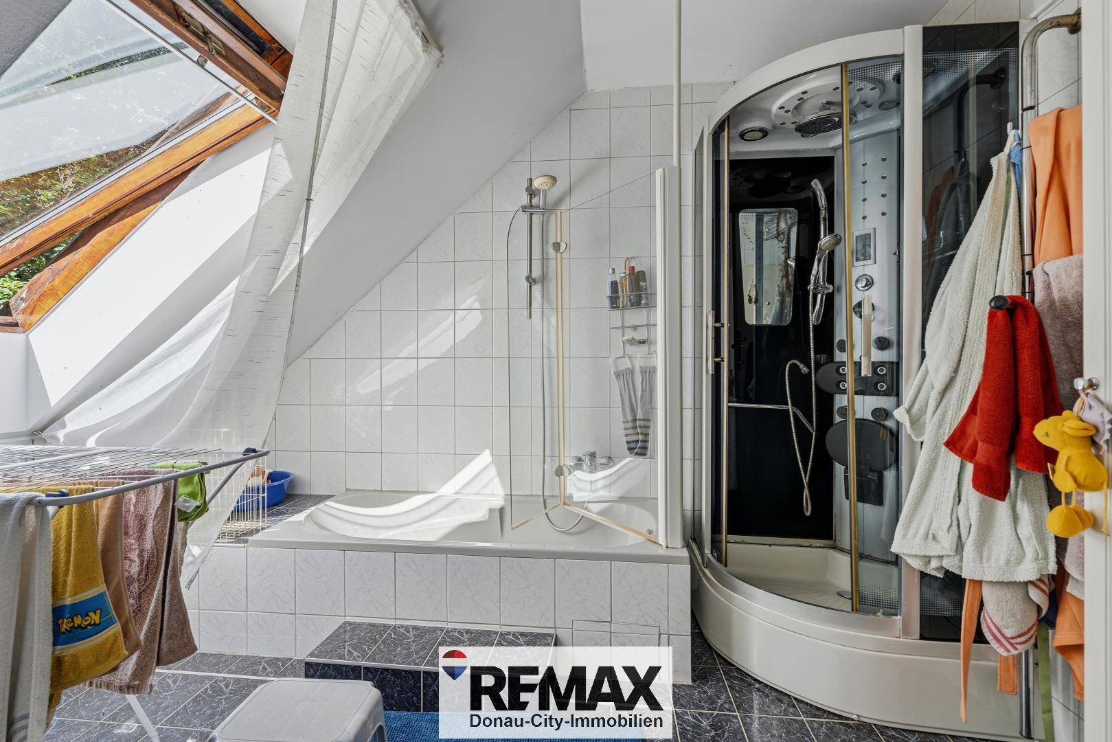 Gefliestes Badezimmer mit Badewanne, Duschkabine und Dachfenster für natürliches Licht.