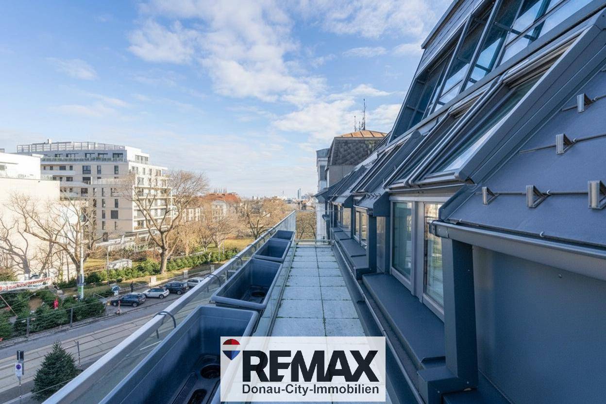 Lange Dachterrasse mit Blick auf die Stadt und umliegende Gebäude unter blauem Himmel.