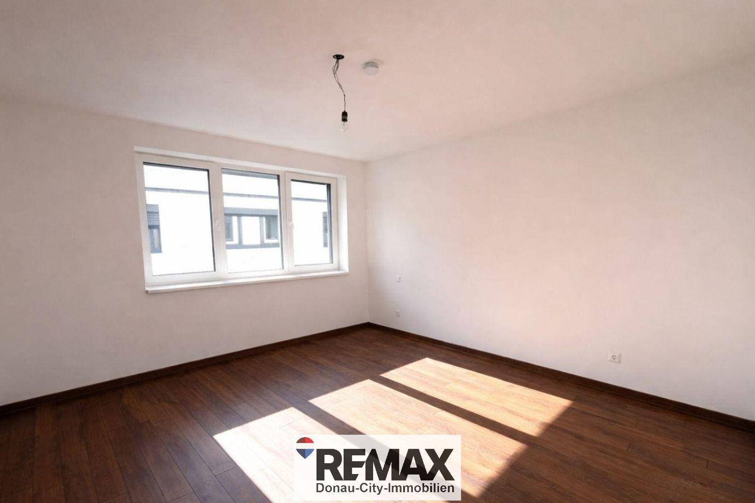 Freundliches Zimmer mit dunklem Holzboden und einem großen Fenster, das für eine helle Atmosphäre sorgt.