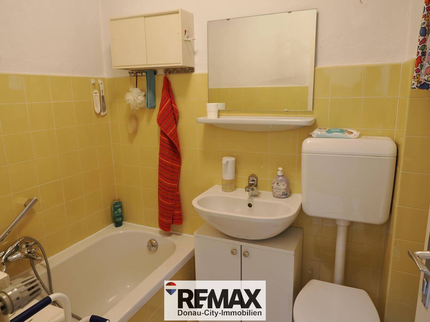 Badezimmer mit gelben Fliesen, Badewanne, Waschbecken und Spiegel.