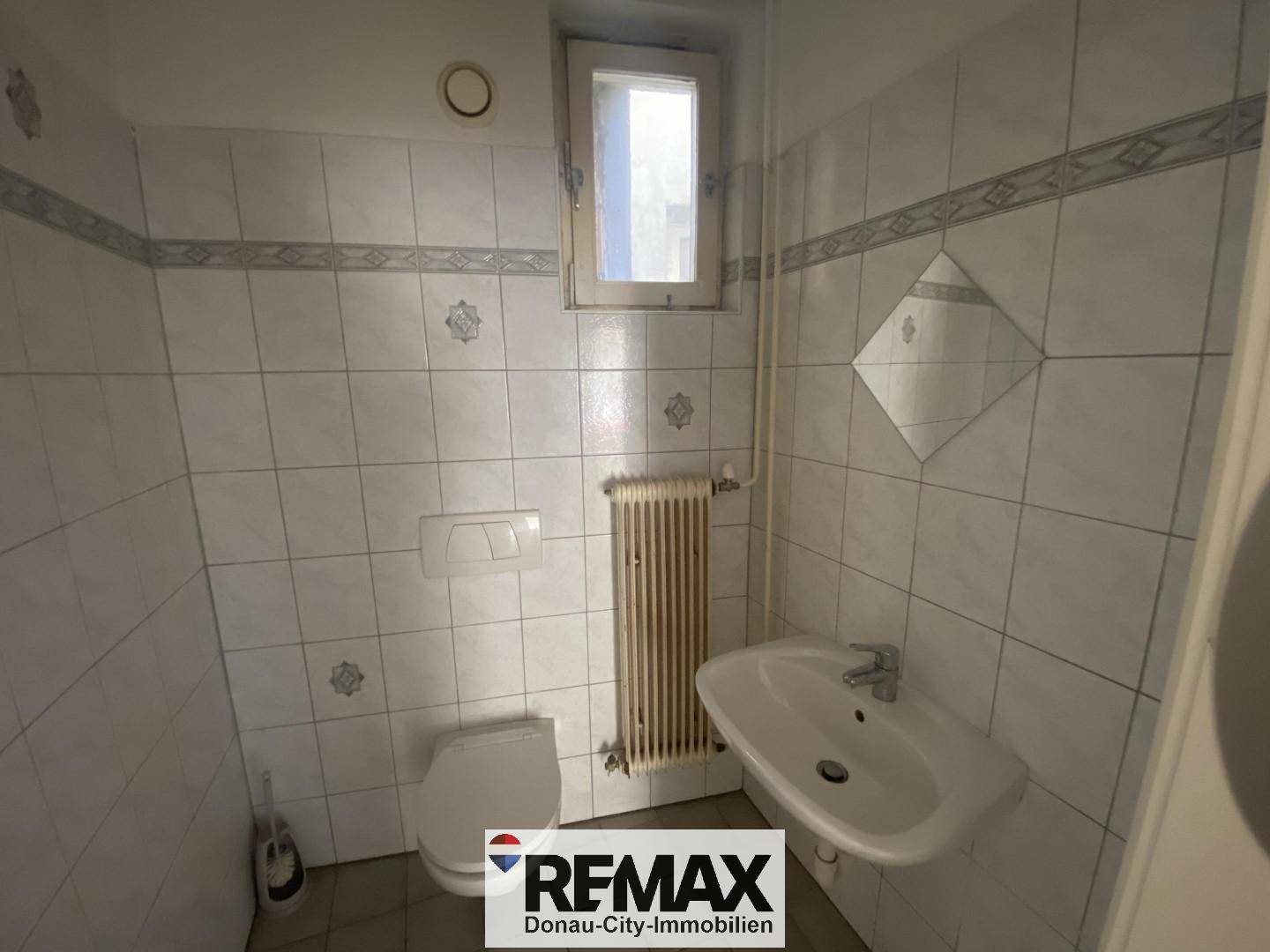 Kleines WC mit Toilette, Waschbecken, Heizkörper und Fenster, komplett gefliest.