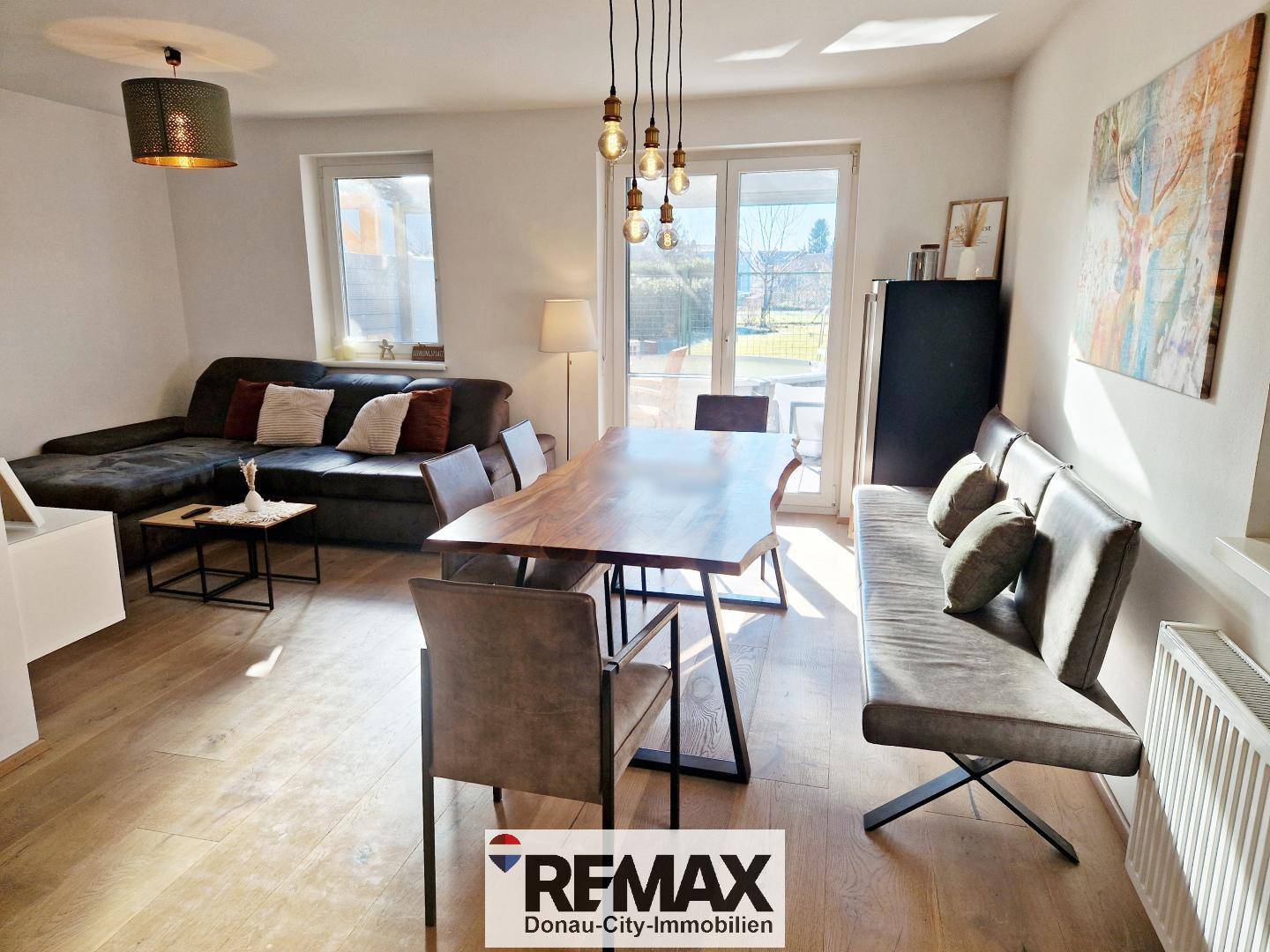Heller offener Wohn-Essbereich mit großem Holztisch, bequemer Couch und Zugang zur Terrasse.