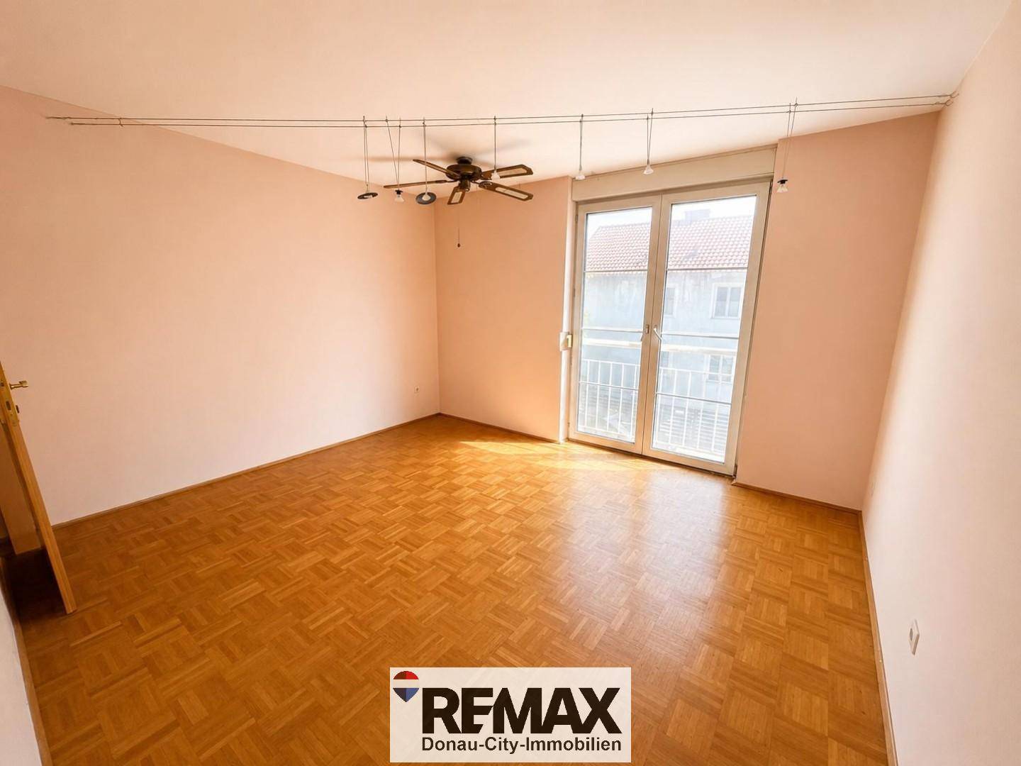 Geräumiges Schlafzimmer mit Parkettboden, hellrosa Wänden und Deckenventilator, mit Balkonzugang.
