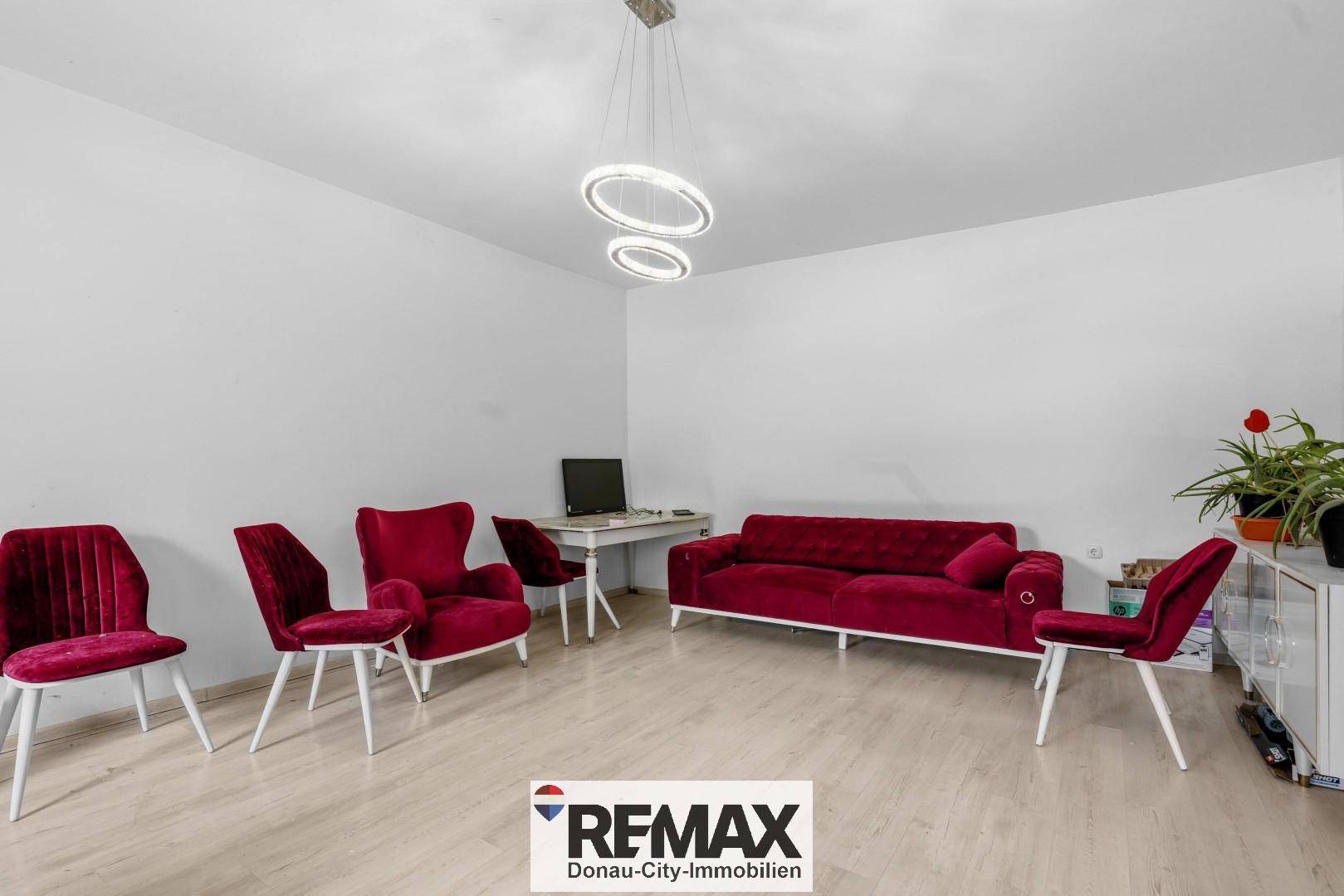 Geräumiges Wohnzimmer mit roter Samtpolsterung, Schreibtisch und modernem Deckenlicht.