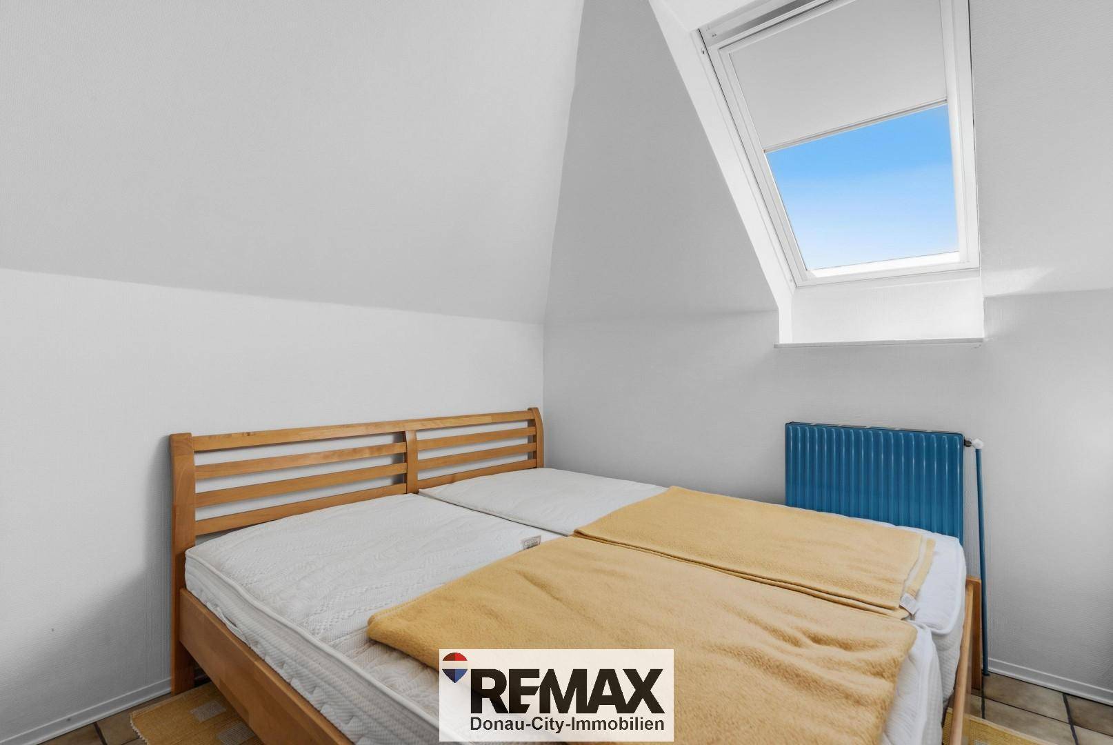 Gemütliches Schlafzimmer im Dachgeschoss mit Holzbett und Dachfenster.