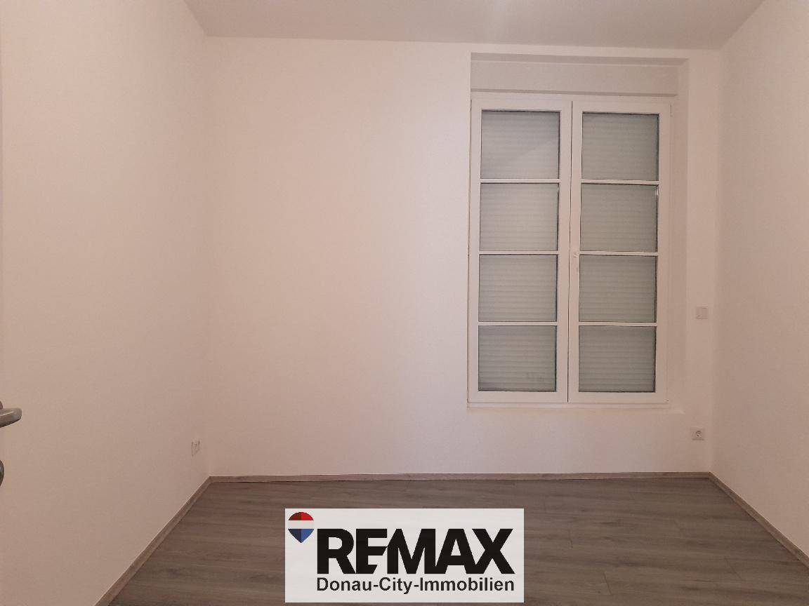 Helles, leeres Zimmer mit großem Fenster und Rollläden, ideal als Schlaf- oder Arbeitszimmer.