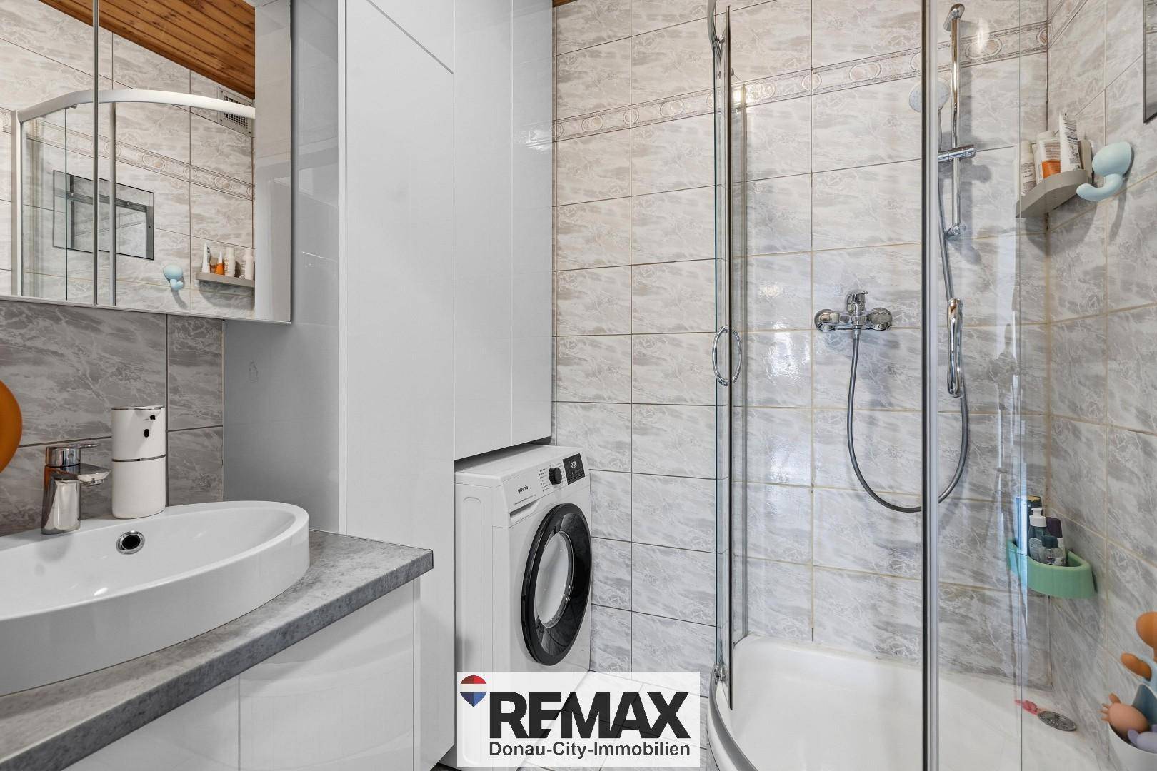 Badezimmer mit Duschkabine, Waschbecken, Spiegelschrank und Waschmaschine.