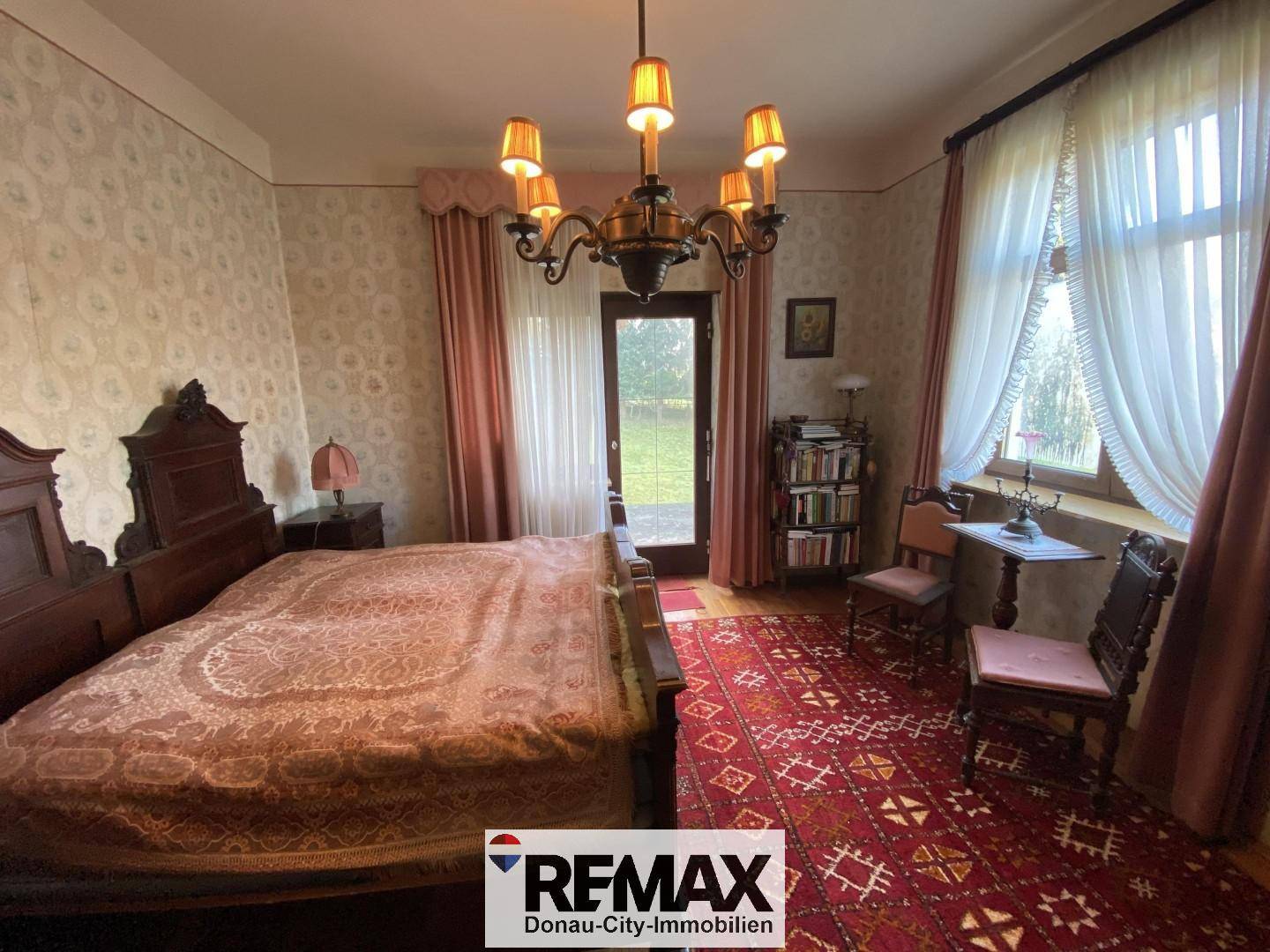 Traditionelles Schlafzimmer mit Doppelbett, gemusterter Tapete und Zugang zum Garten.