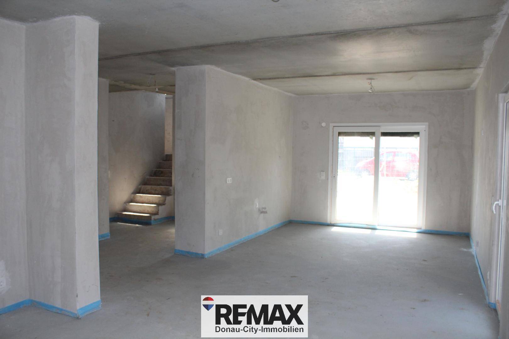 Großer, heller Raum im Rohbau mit Betonboden und sichtbarer Treppe, ideal für individuelle Gestaltung.