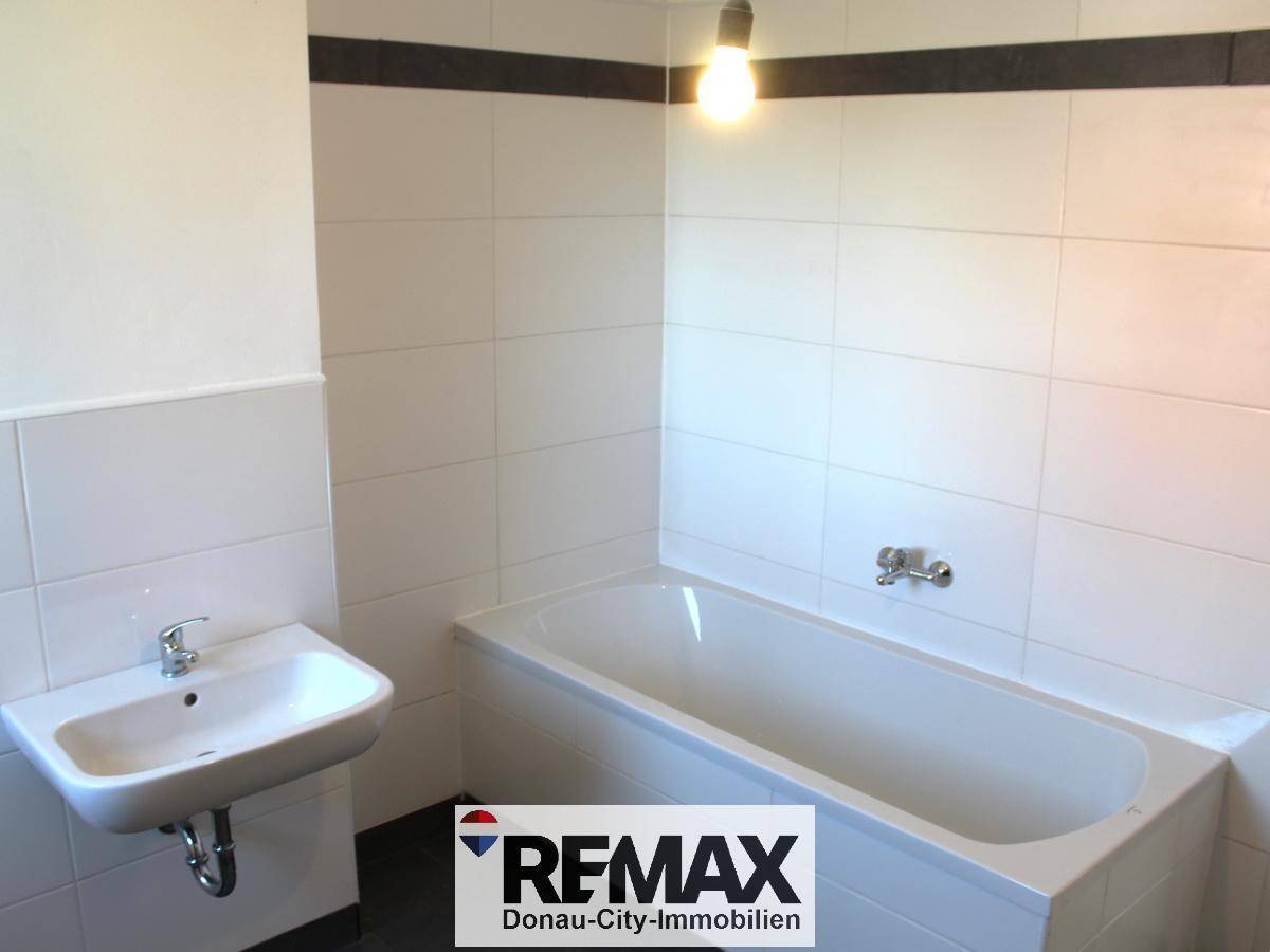 Funktionales Badezimmer mit weiß gefliesten Wänden, Badewanne und einem einzelnen Waschbecken.
