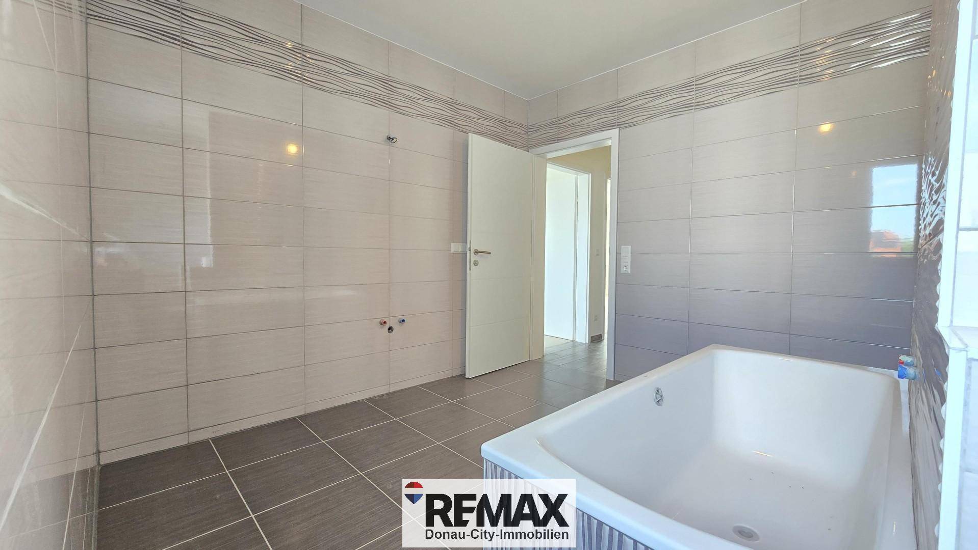 Geräumiges Badezimmer mit Badewanne, grauen Fliesen und einem Fenster für Tageslicht.