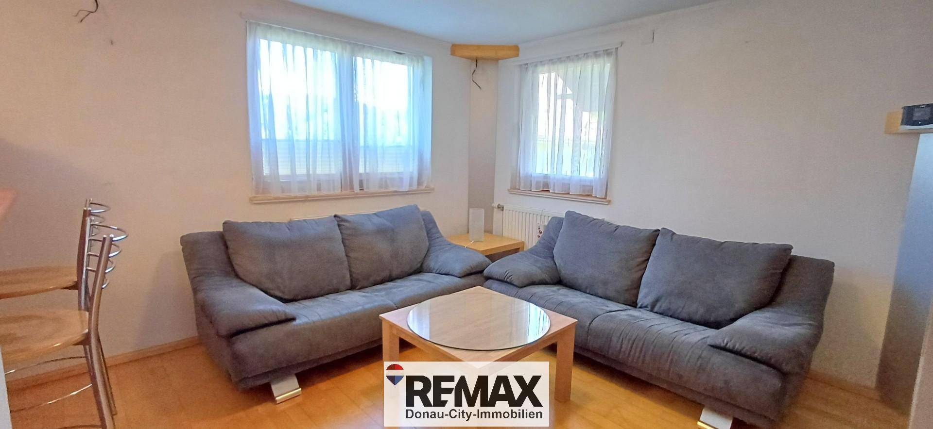 Gemütliches Wohnzimmer mit zwei grauen Sofas, Couchtisch und hellen Fenstern.