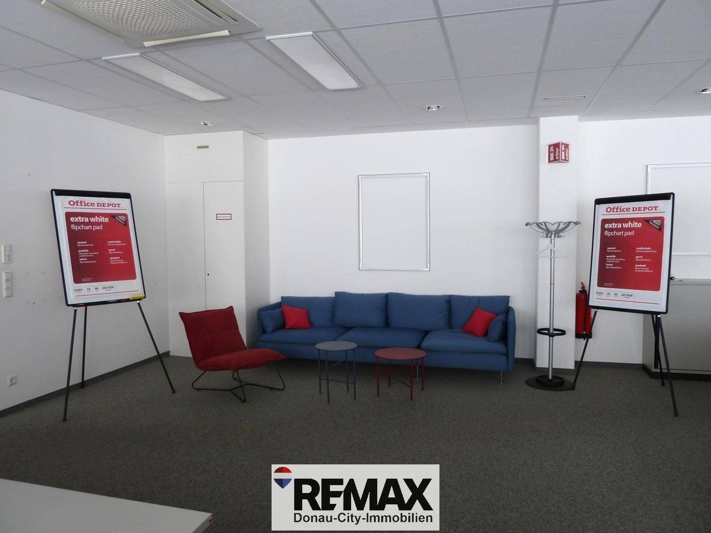 Gemütlicher Loungebereich mit blauem Sofa, rotem Sessel und Beistelltischen auf Teppichboden.