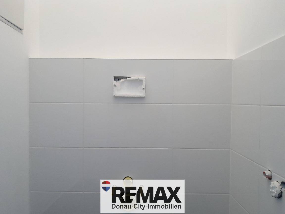 Bereich für ein wandmontiertes WC mit grauen Fliesen und vorbereiteten Anschlüssen.