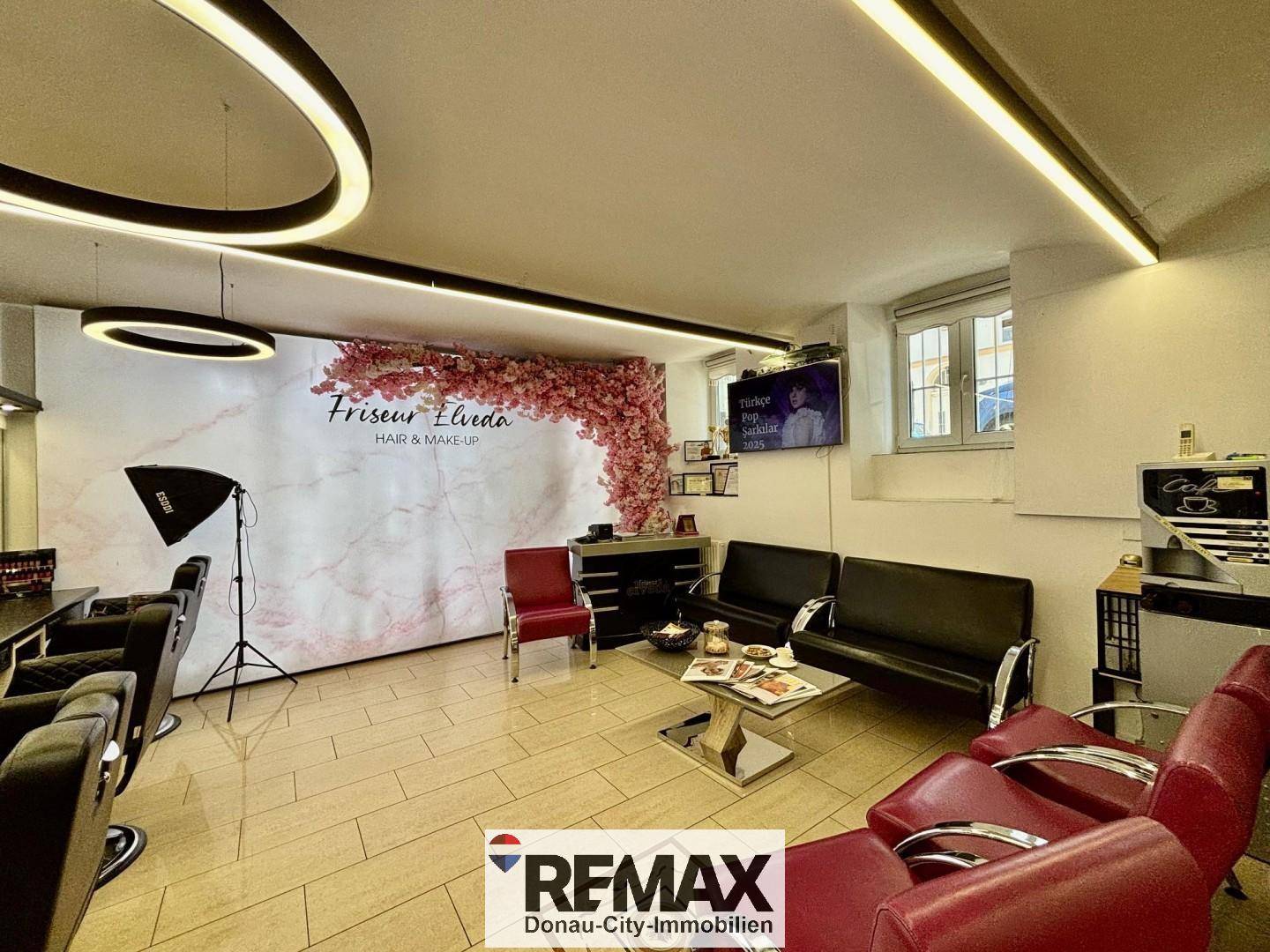 Wartebereich im Friseursalon mit bequemen Sofas, einem Couchtisch und einer stilvollen Wanddekoration.