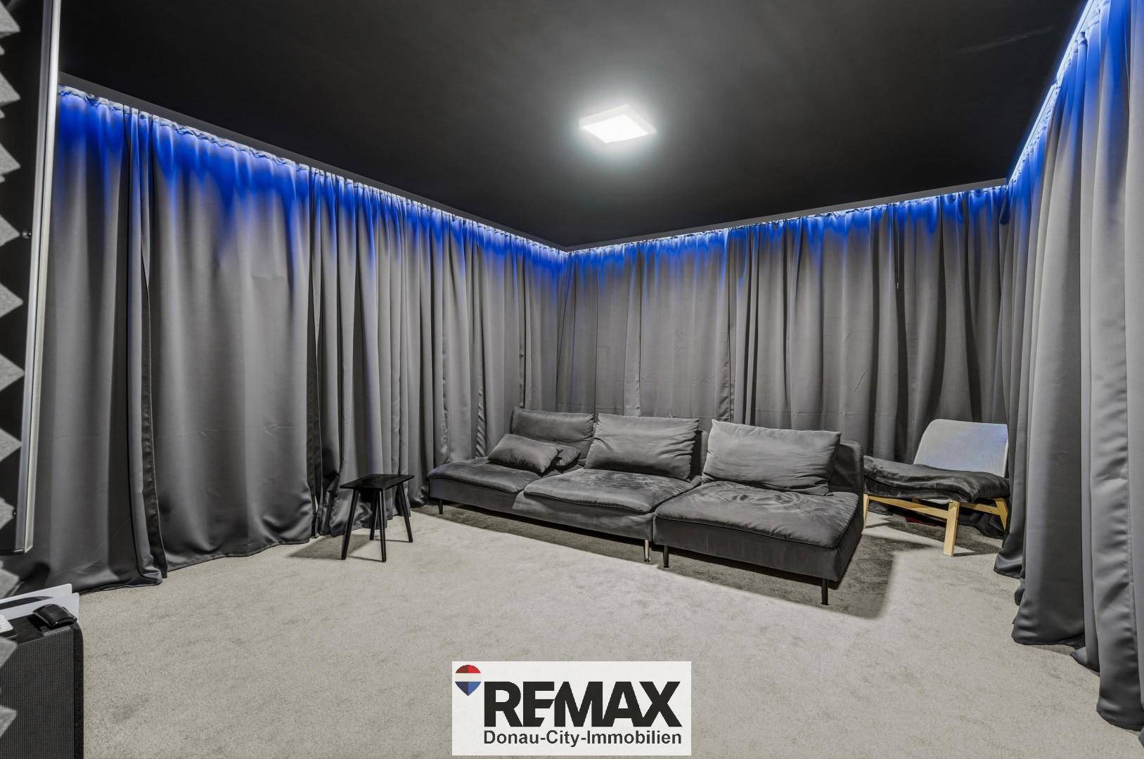 Dunkler Medienraum mit bequemer Couch, Teppichboden und indirekter blauer Beleuchtung.
