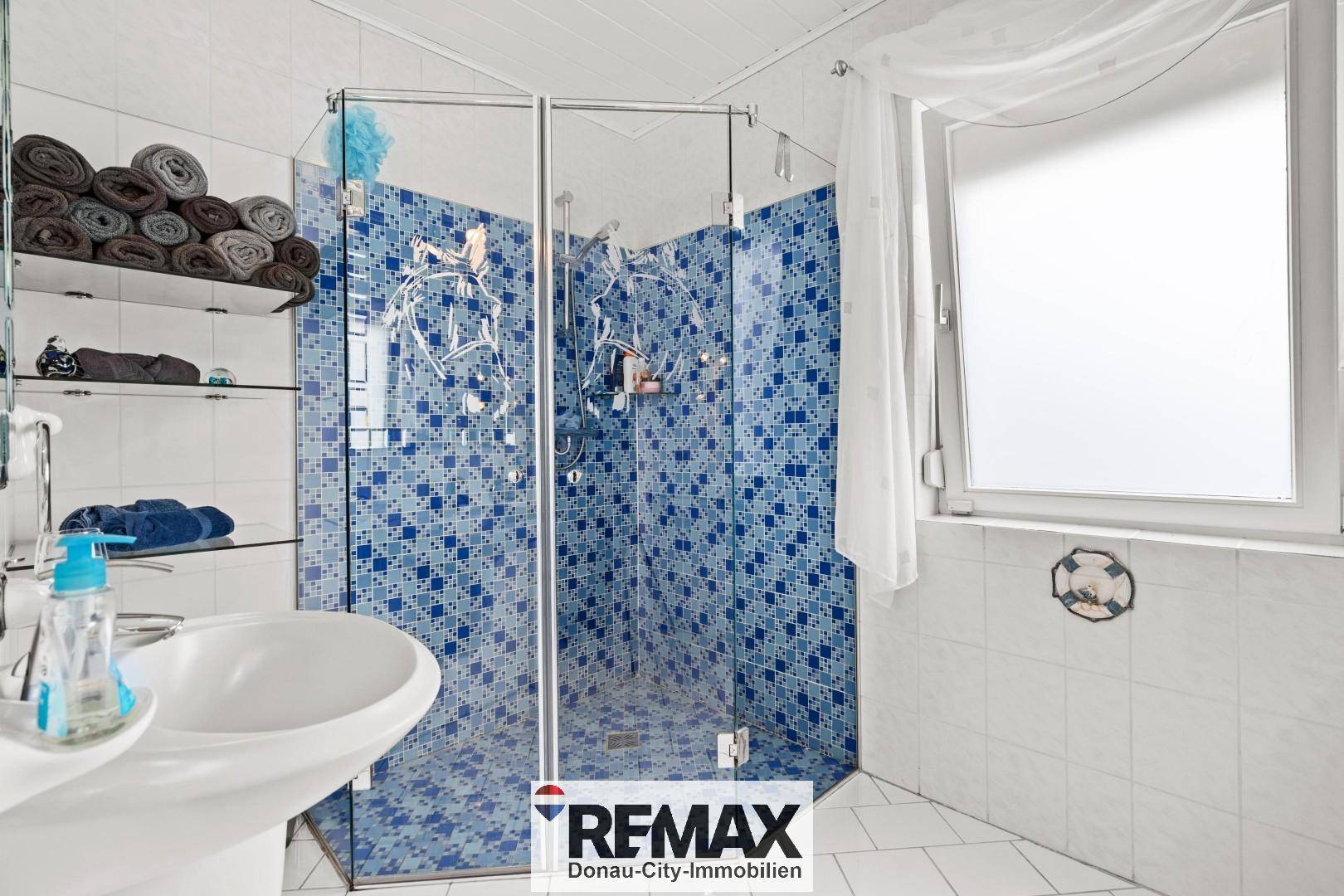 Modernes Badezimmer mit blauen Mosaikfliesen, Duschkabine und Fenster für natürliche Belüftung.