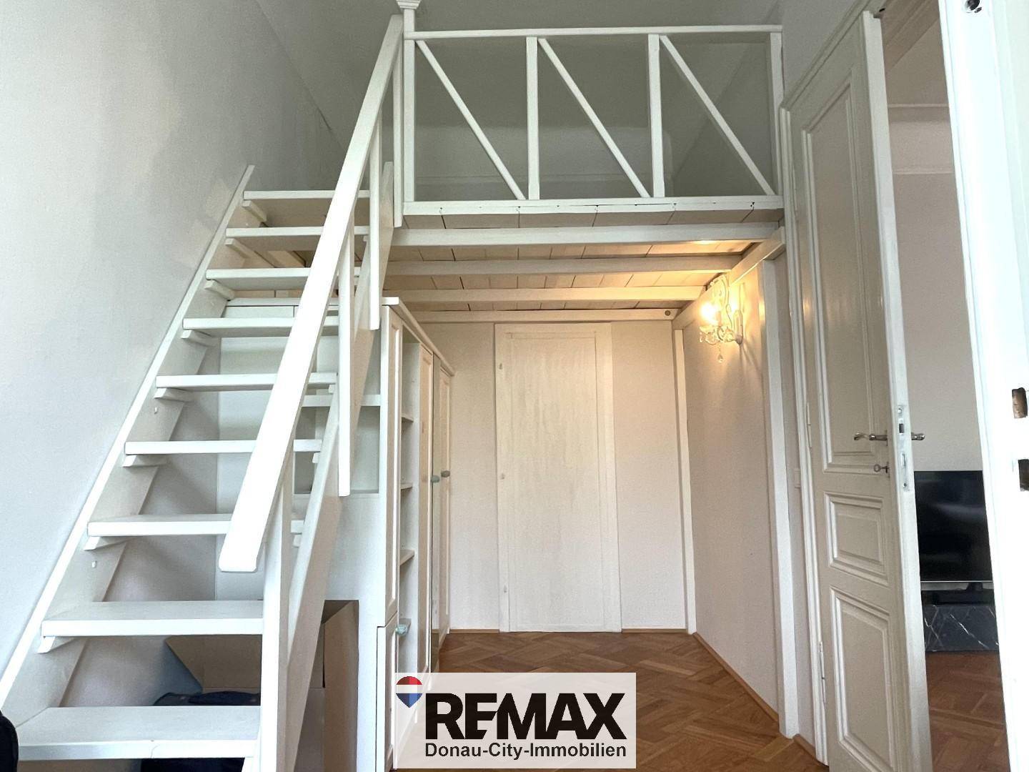 Heller Flur mit Holztreppe, die zu einem oberen Bereich führt, und hohen Decken.