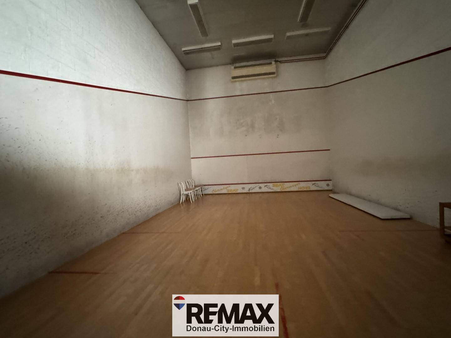 Geräumiger Squash-Court mit Holzboden und weißen Wänden, markiert mit roten Linien für das Spiel.