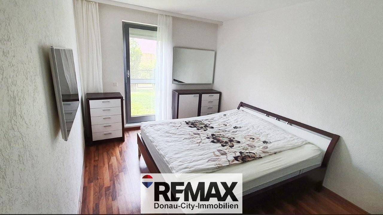 Schlafzimmer mit Holzboden, Doppelbett und Zugang zu einem Außenbereich durch die Fenstertür.