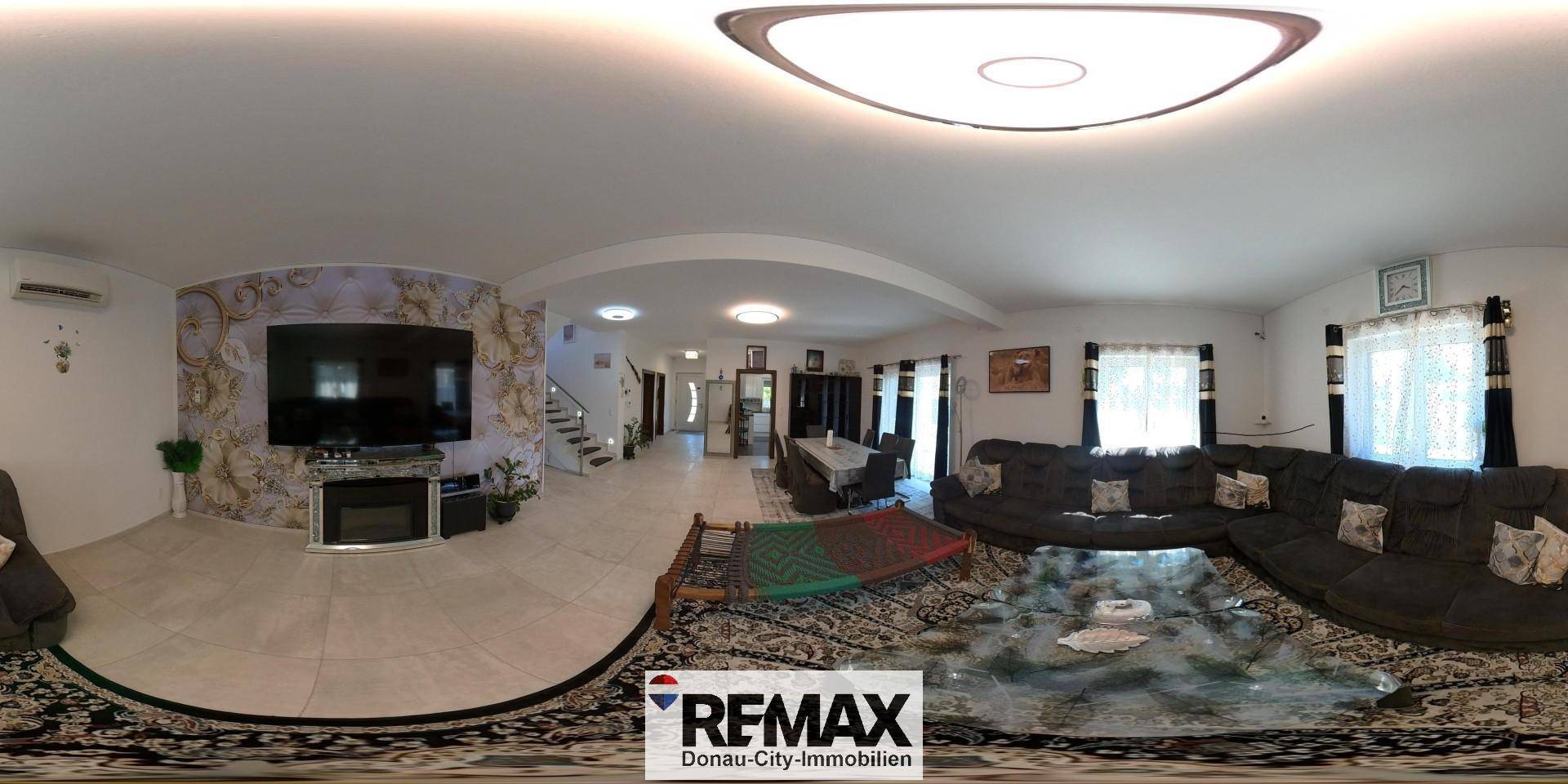 Geräumiges Wohnzimmer mit großem Sofa, Kamin und Fliesenboden, in einem 360-Grad-Panorama.