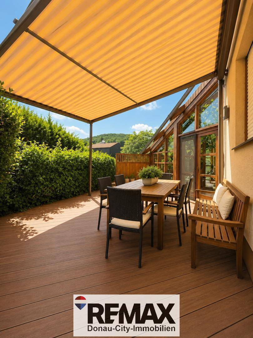 Überdachte Terrasse mit Holzboden, Esstisch und Stühlen, umgeben von grünen Hecken für Privatsphäre.