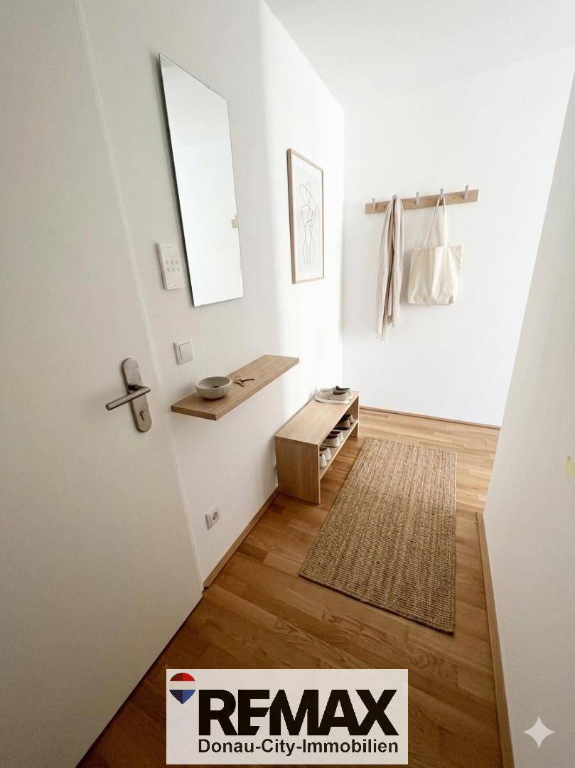 Heller Eingangsbereich mit Holzparkettboden, Garderobe und einem großen Wandspiegel.