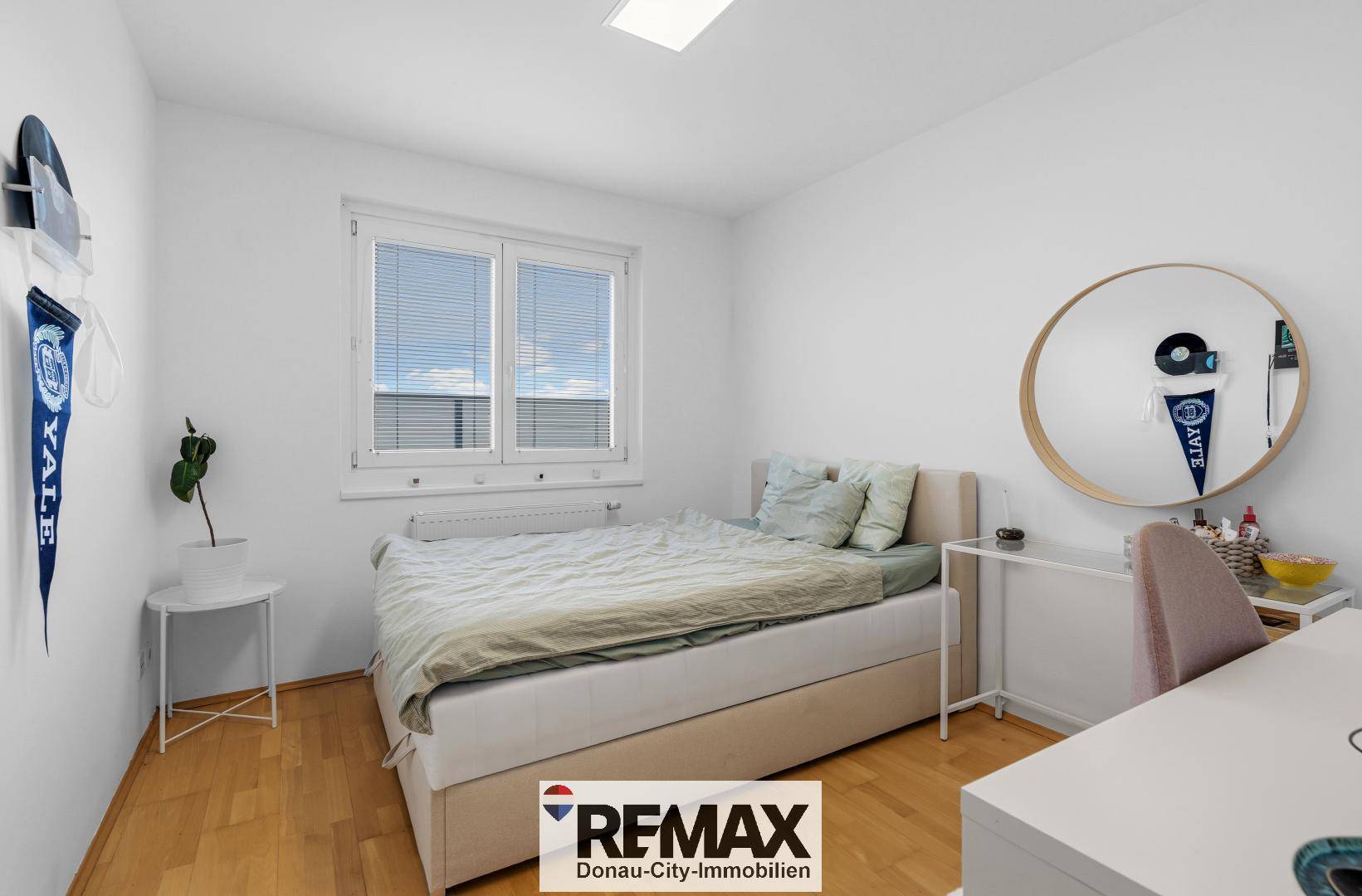 Helles Schlafzimmer mit Holzboden, großem Fenster und minimalistischer Einrichtung.