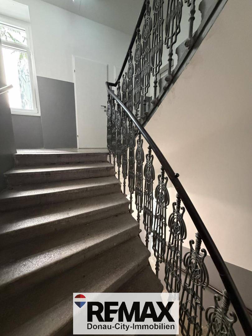 Historisches Treppenhaus mit kunstvollem Metallgeländer und Steinstufen, gut beleuchtet durch ein Fenster.