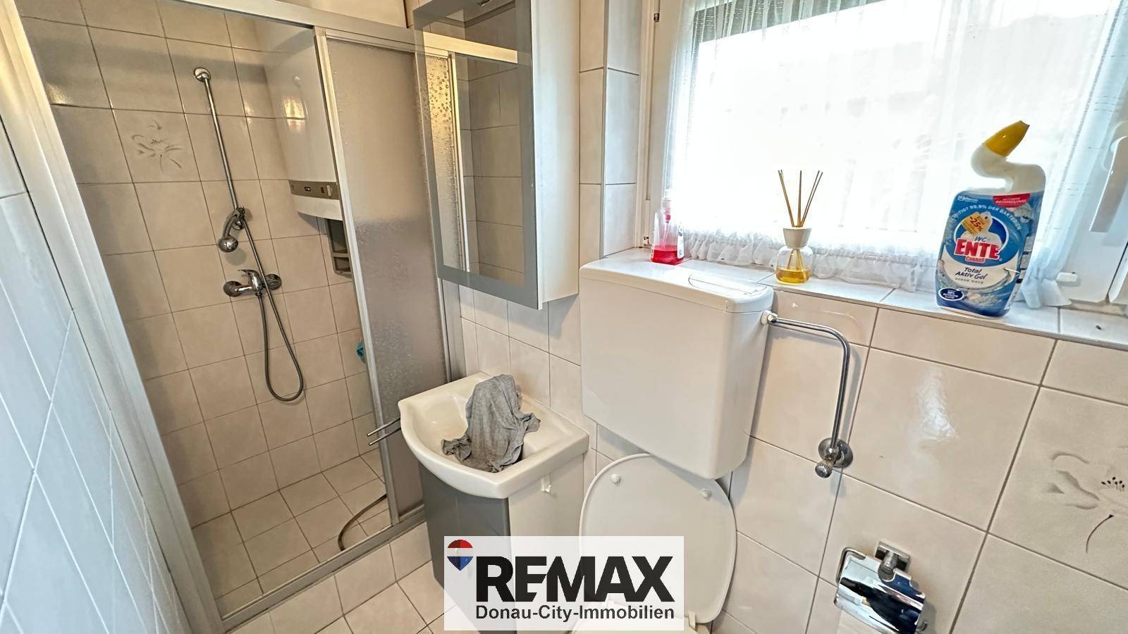 Kleines Badezimmer mit Dusche, Toilette, Waschbecken und Fliesenboden.