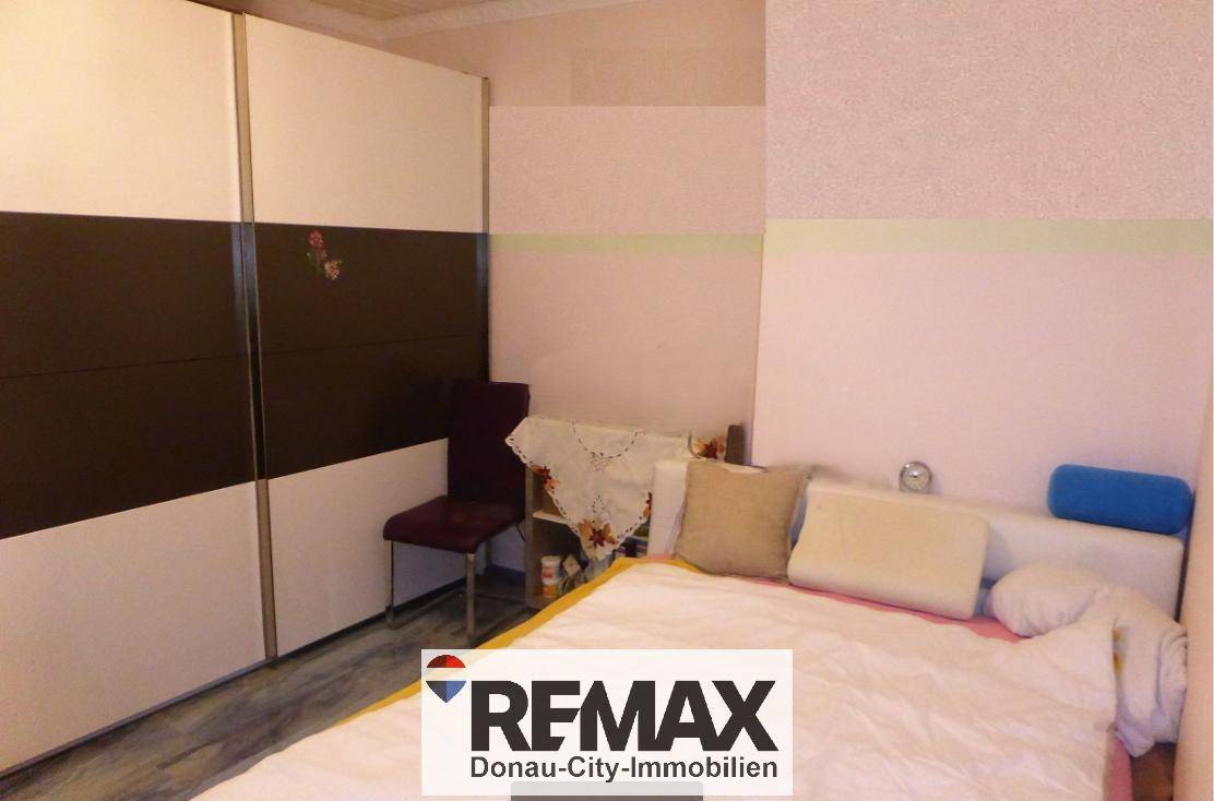 Schlafzimmer mit großem Schiebetürenschrank und hellem Bett, mit Laminatboden.