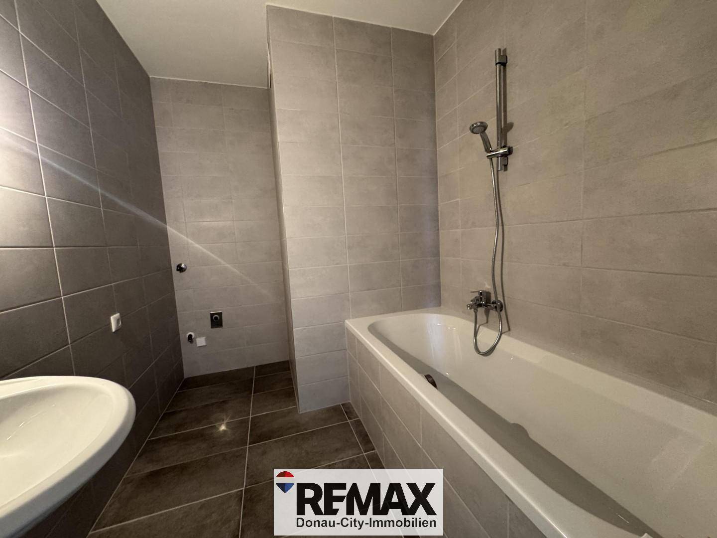 Modern gefliestes Badezimmer mit Badewanne, Duscharmatur und einem einzelnen Waschbecken.