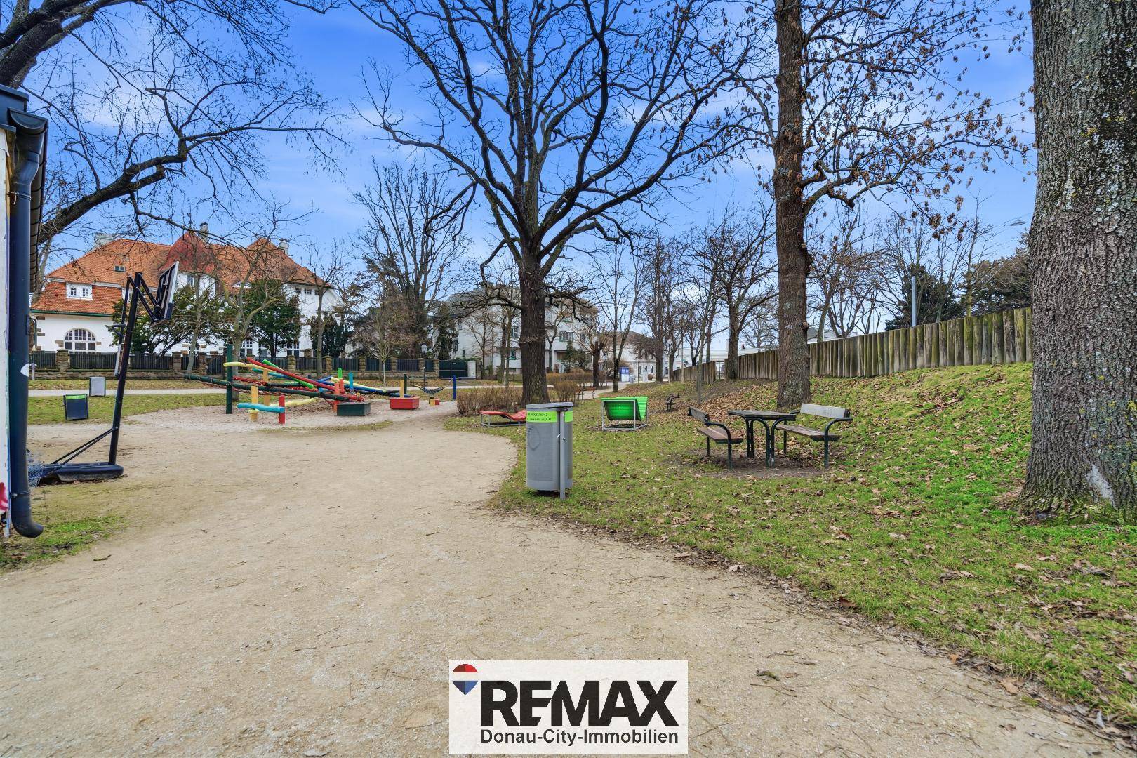 Öffentlicher Spielplatz in einem Park mit Bäumen und Spielgeräten.