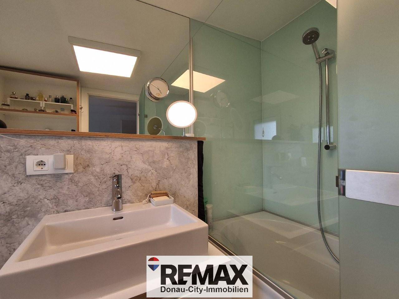 Helles Badezimmer mit moderner Dusche, Glasabtrennung und Waschtisch.