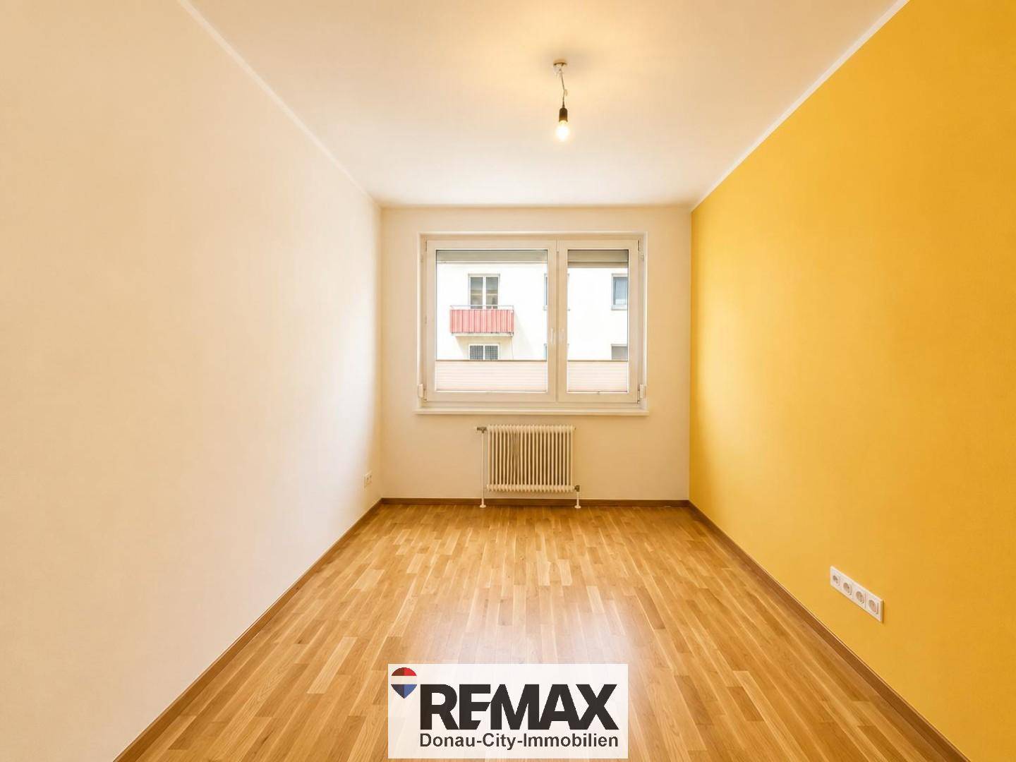 Helles Schlafzimmer mit Parkettboden und einer sonnigen gelben Akzentwand, ideal für ein Kinderzimmer.