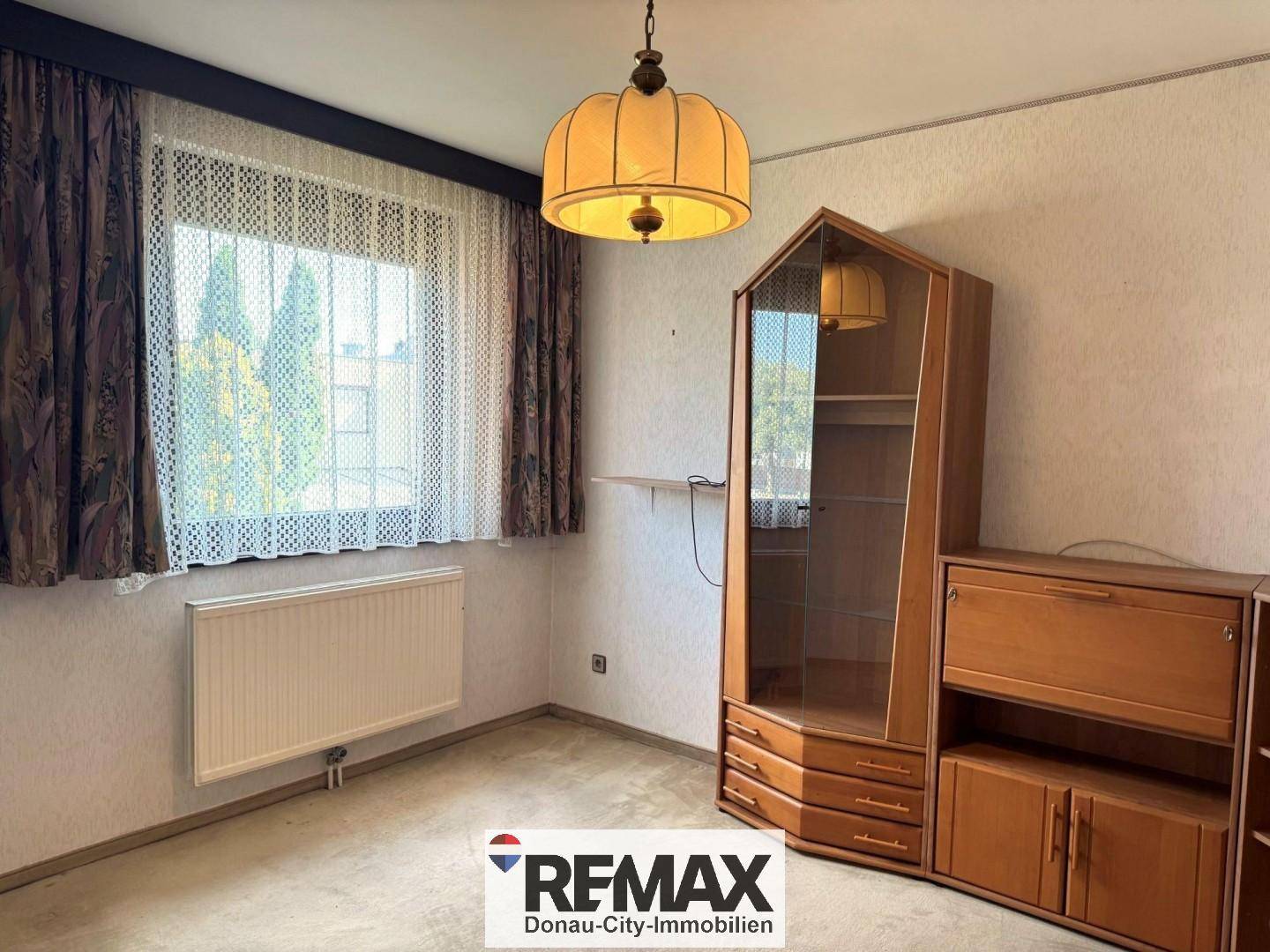 Helles Zimmer mit Teppichboden, großem Fenster und traditionellen Holzmöbeln.